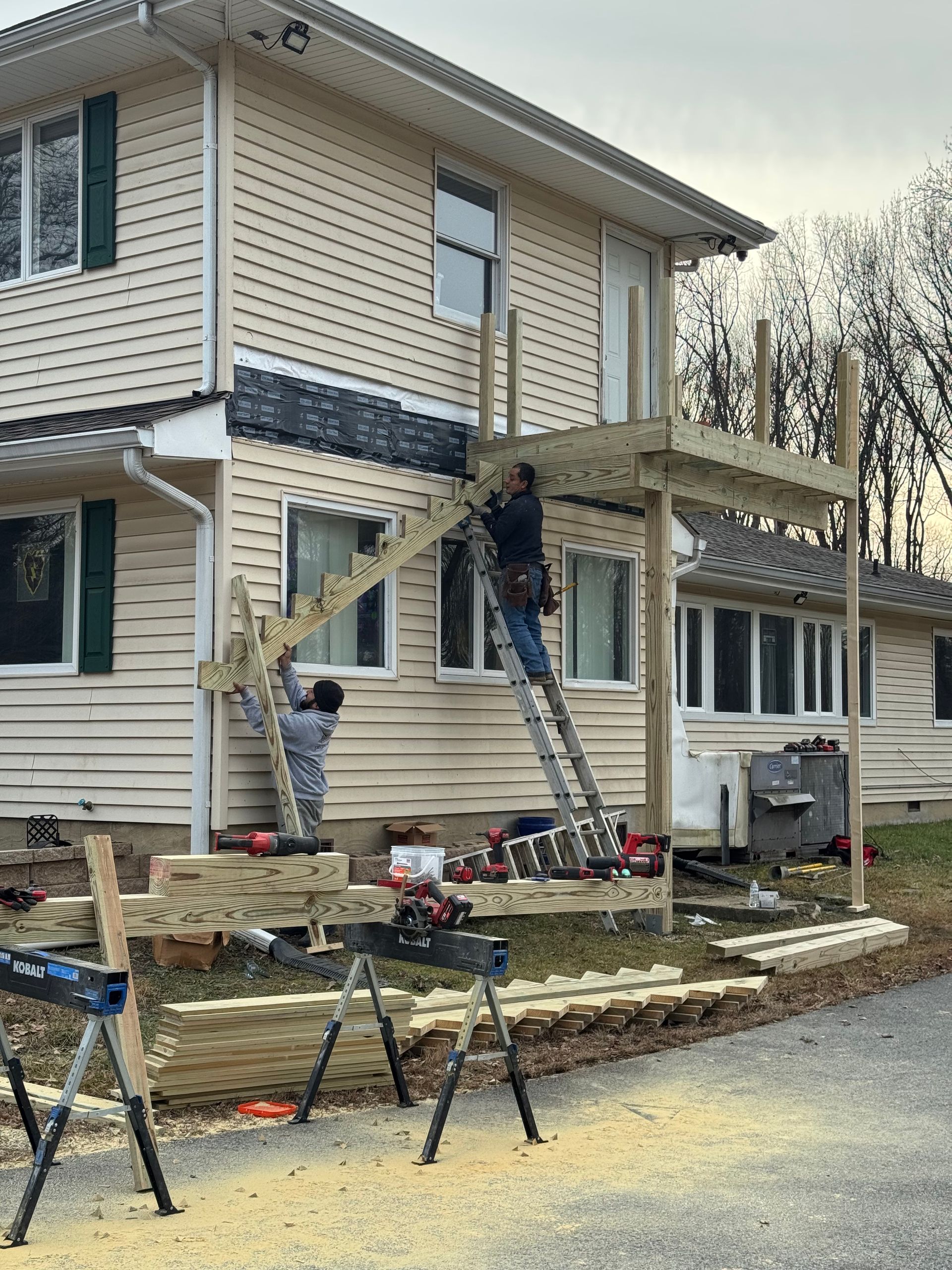 Workers on ladders repairing the exterior of a two-story house with siding and scaffolding in front.