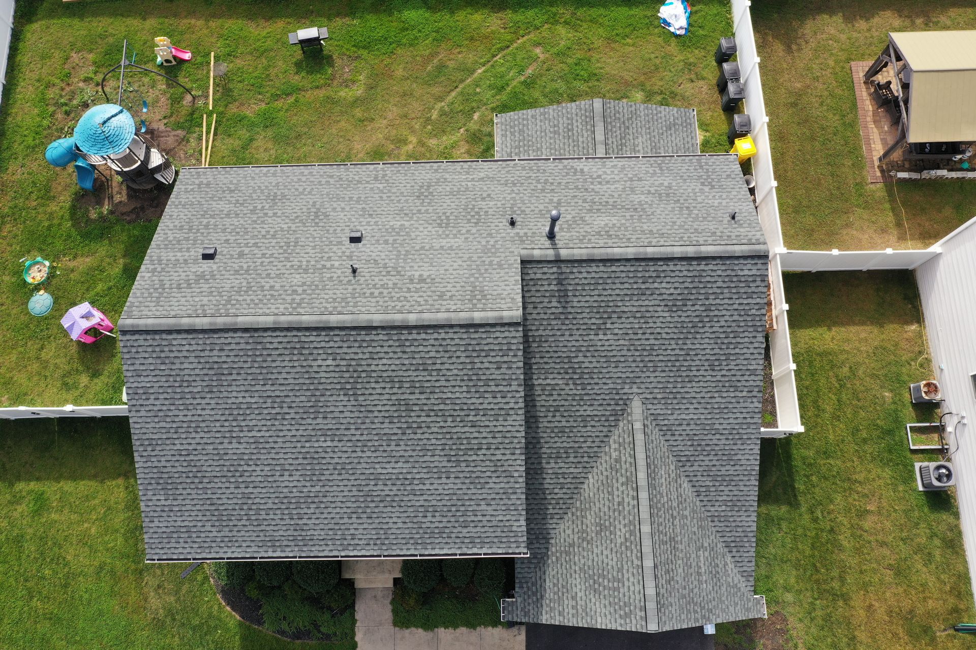 Aerial view of a gray shingled house roof with a front porch and lawn around it.