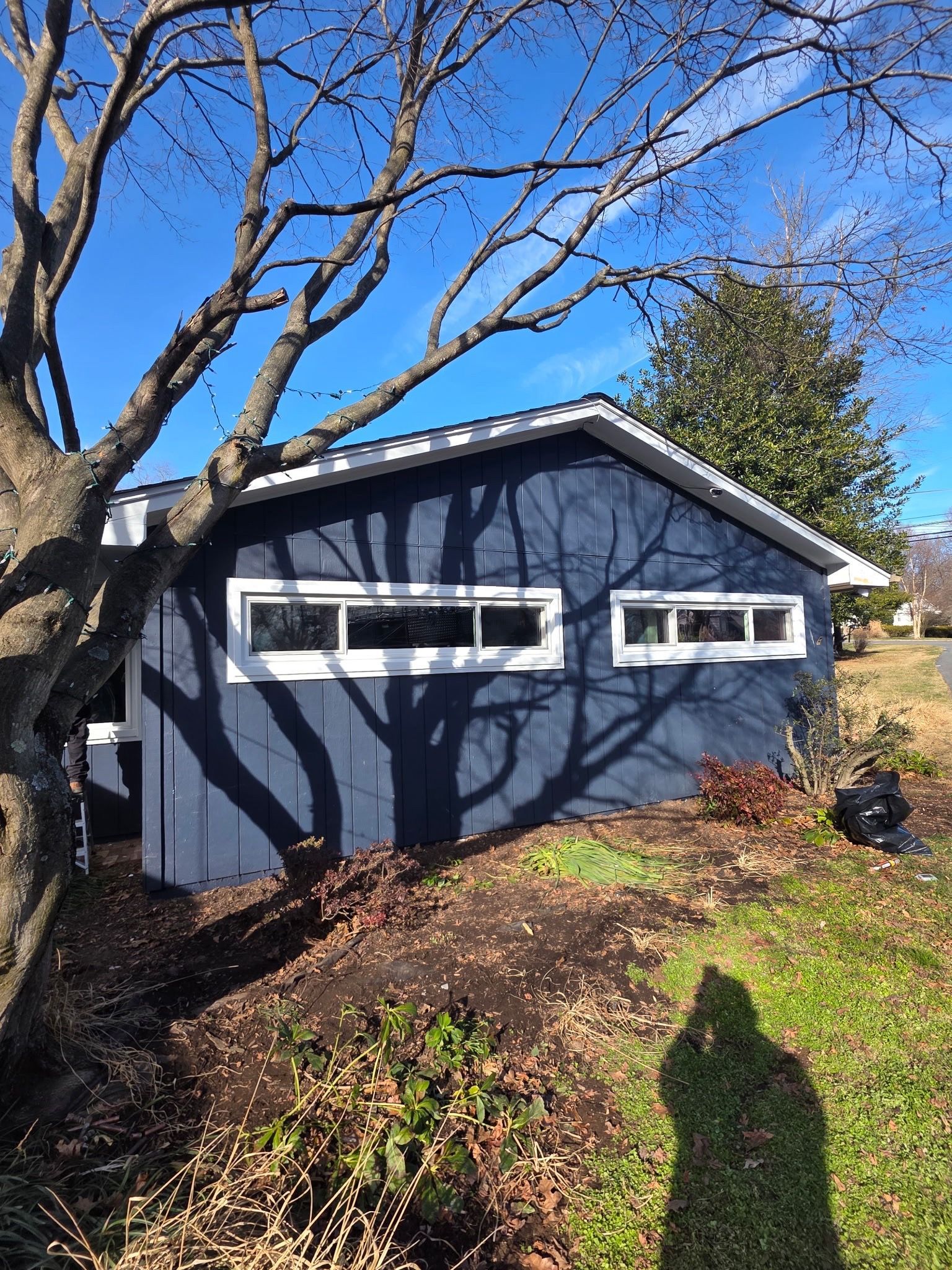 Blue garage with white trim and windows, framed by tree shadows on a sunny day.