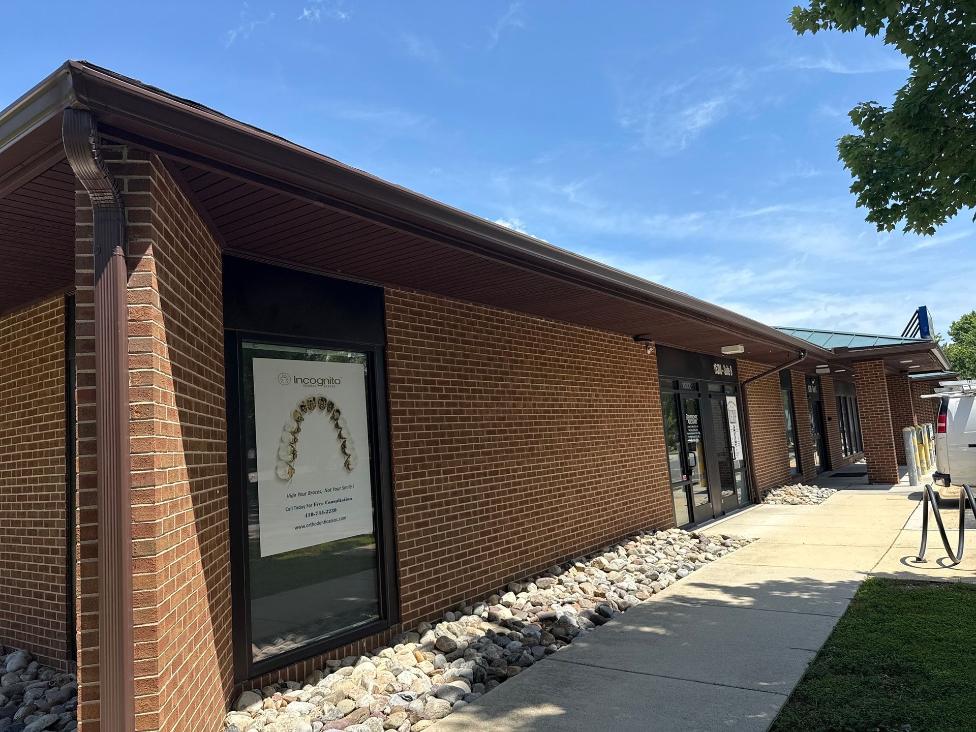 Brick building with large windows and a sidewalk under a blue sky, with a sign by the entrance