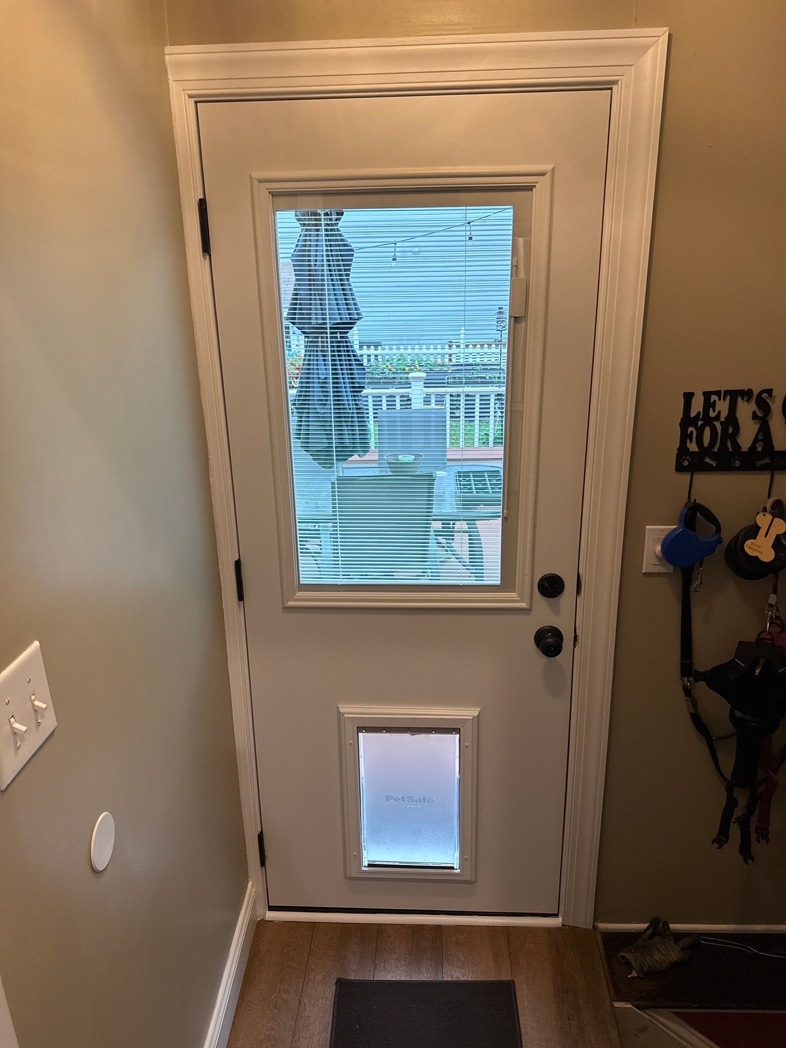 Interior white door with a window, pet flap, and holiday wreath hanging on the wall nearby.