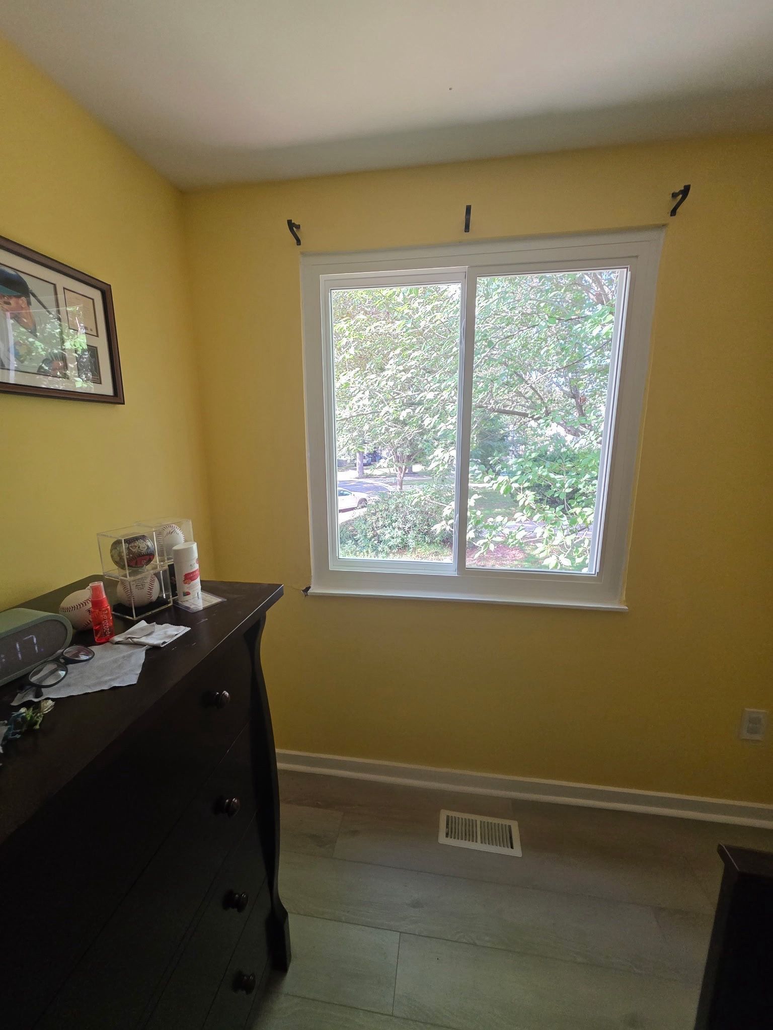 Yellow bedroom with a window, dresser, and beige carpet, lit by daylight.