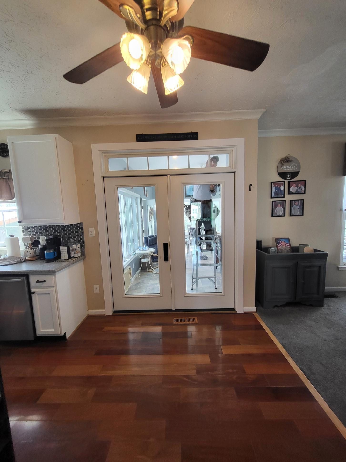 Living room with ceiling fan, hardwood floor, French doors, and kitchen cabinets visible to the left