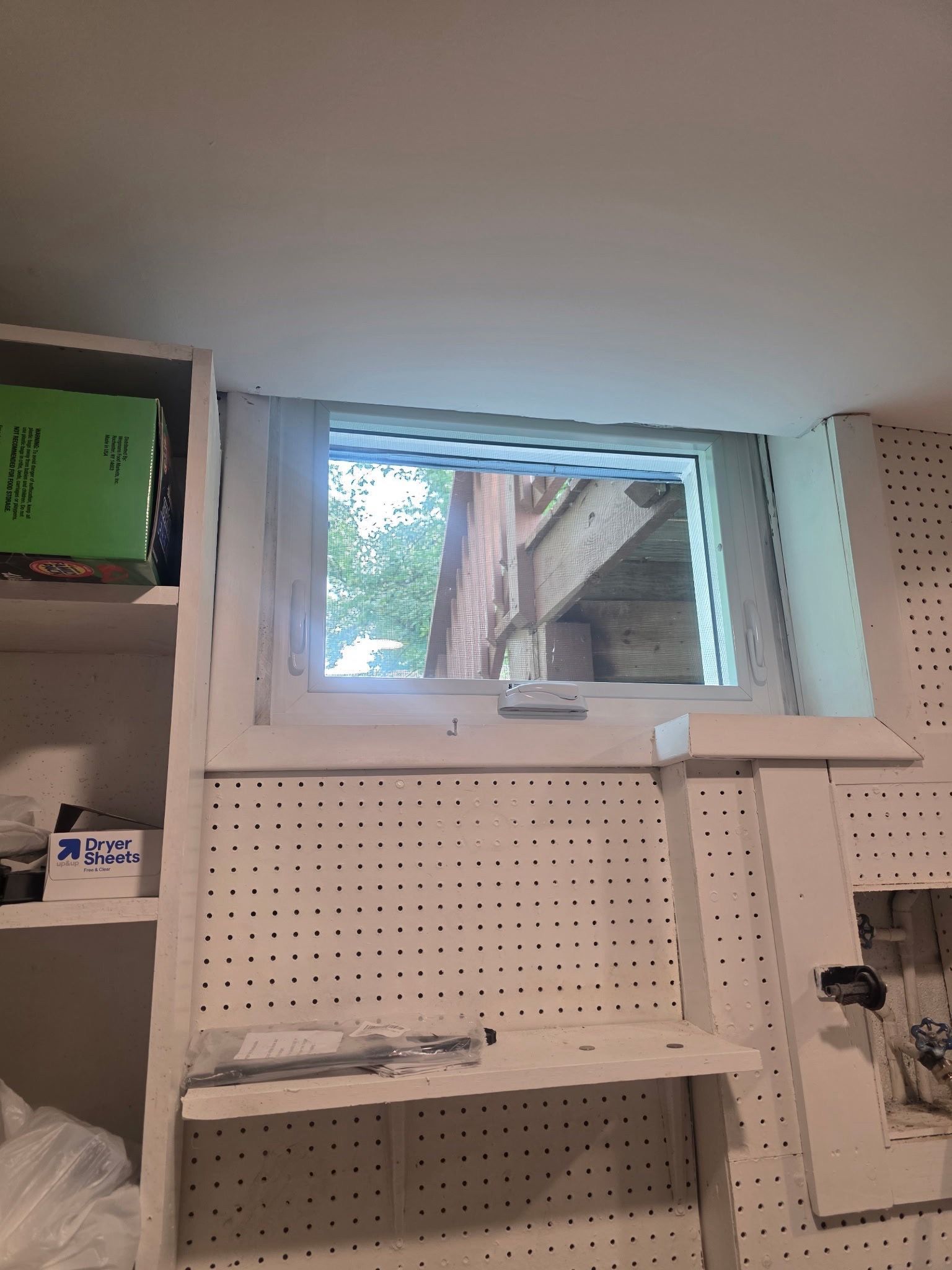 Pegboard wall with shelves and a small open window in a utility room