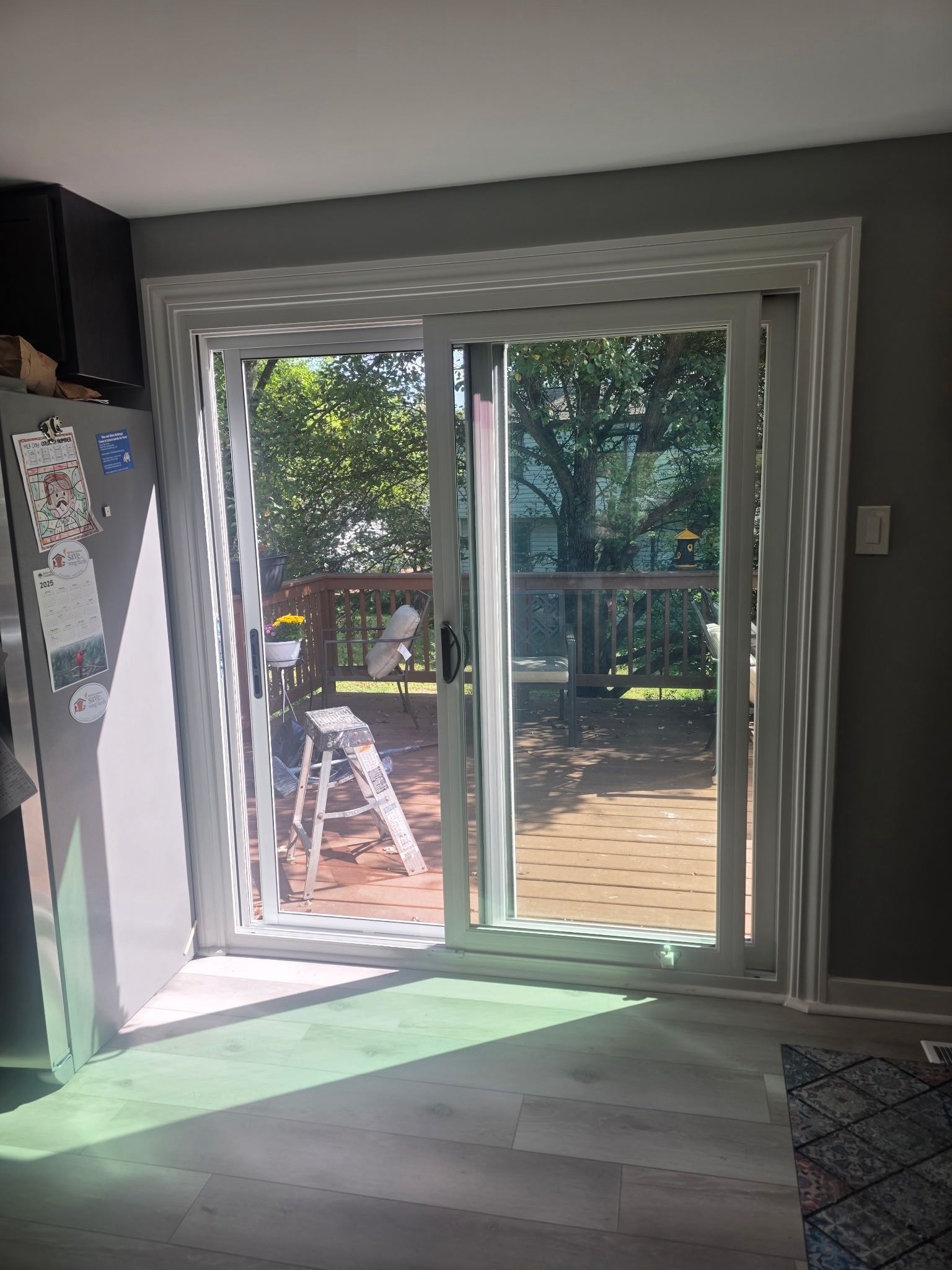 Sunlit sliding glass doors opening to a backyard deck and trees from a dim interior room