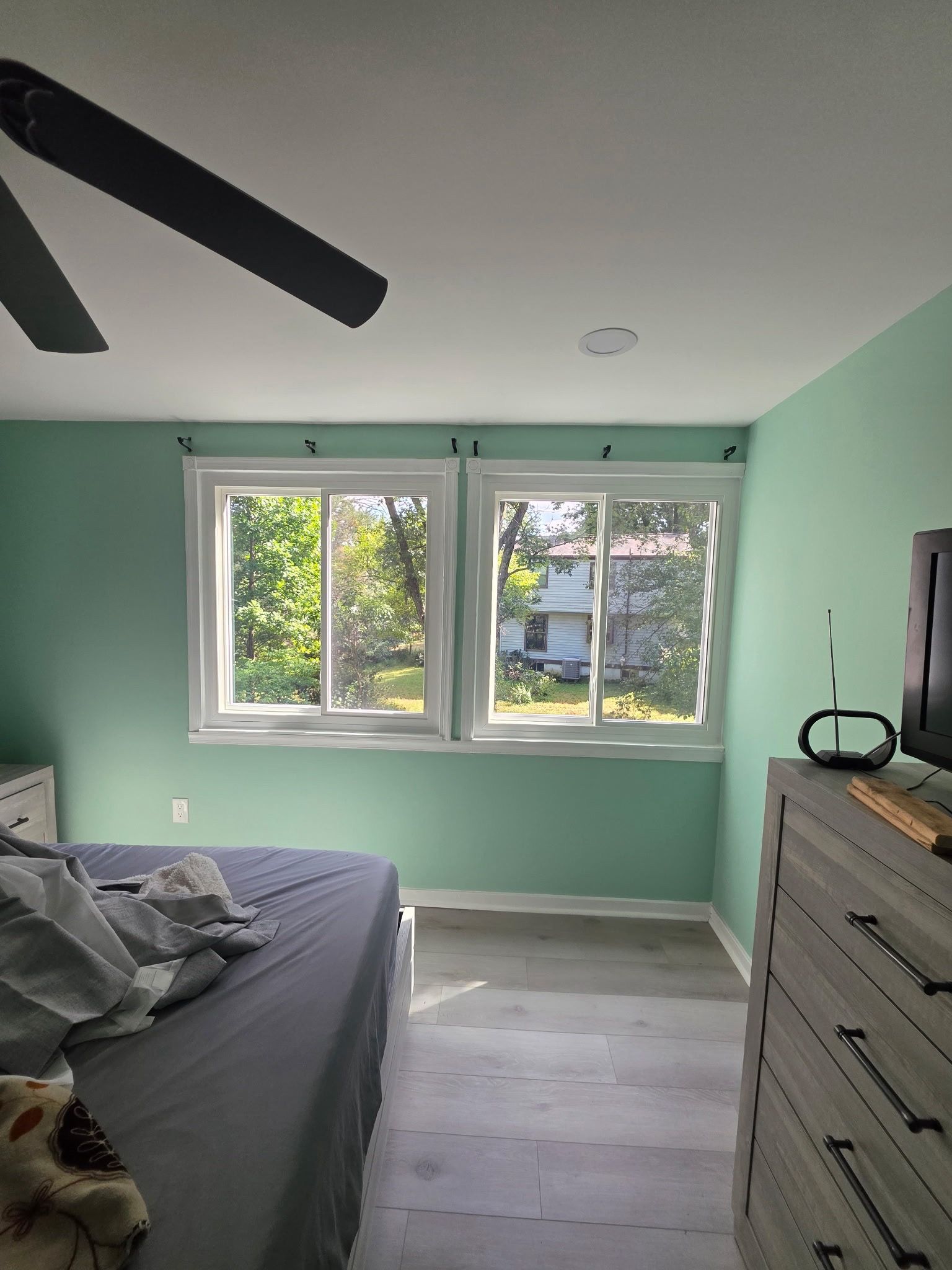 Small mint-green bedroom with a bed, dresser, ceiling fan, and window view.