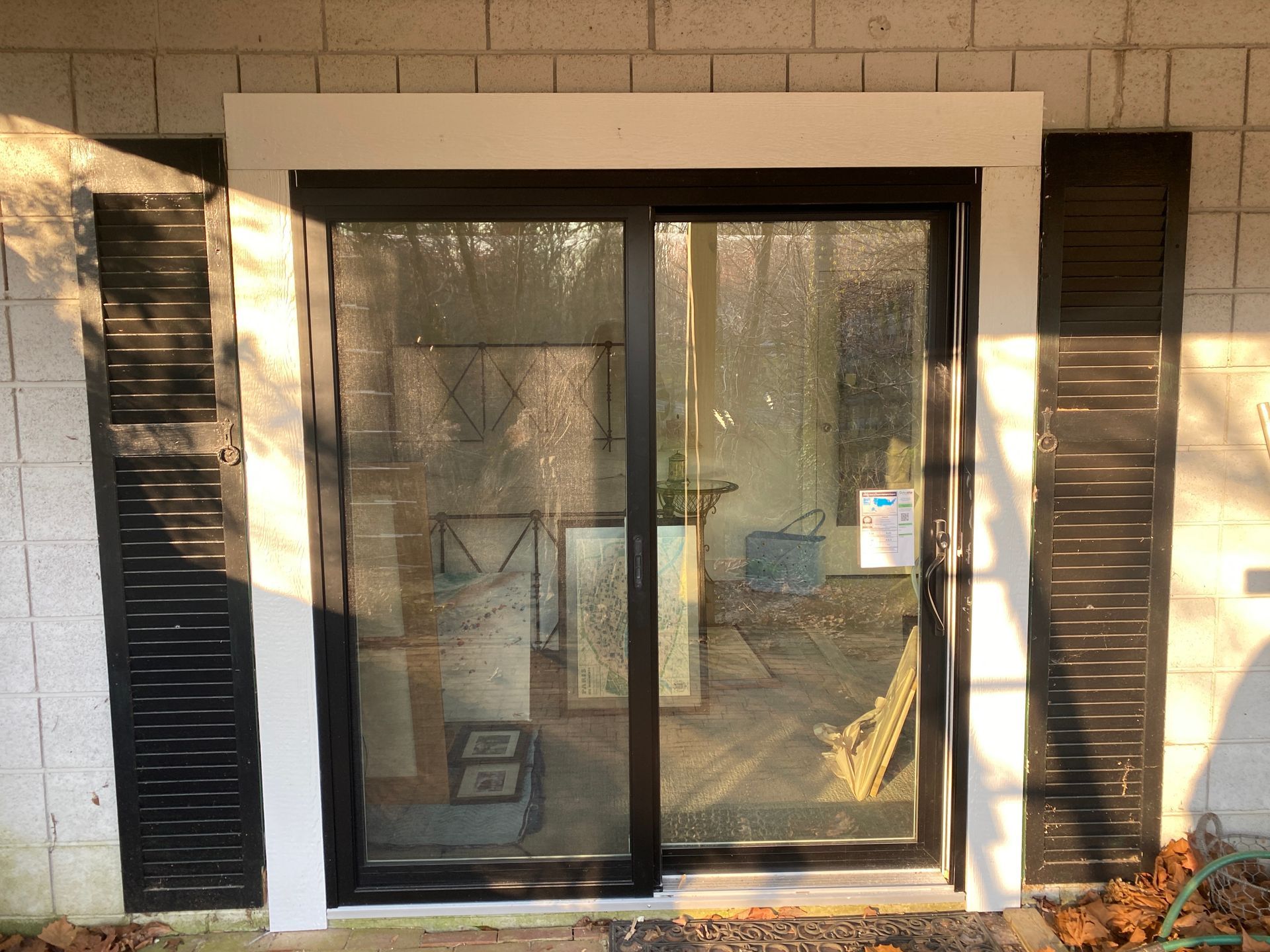 Sliding glass patio door with white frame and black shutters on a brick exterior