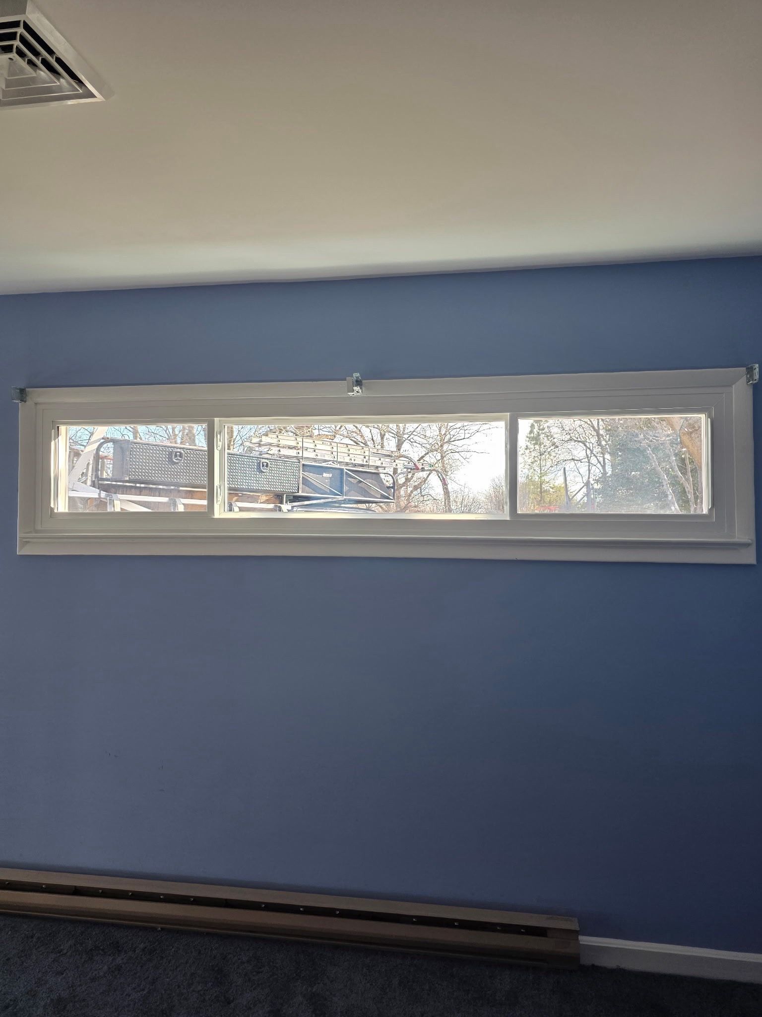 Blue room wall with a long horizontal window and white trim, showing trees outside.