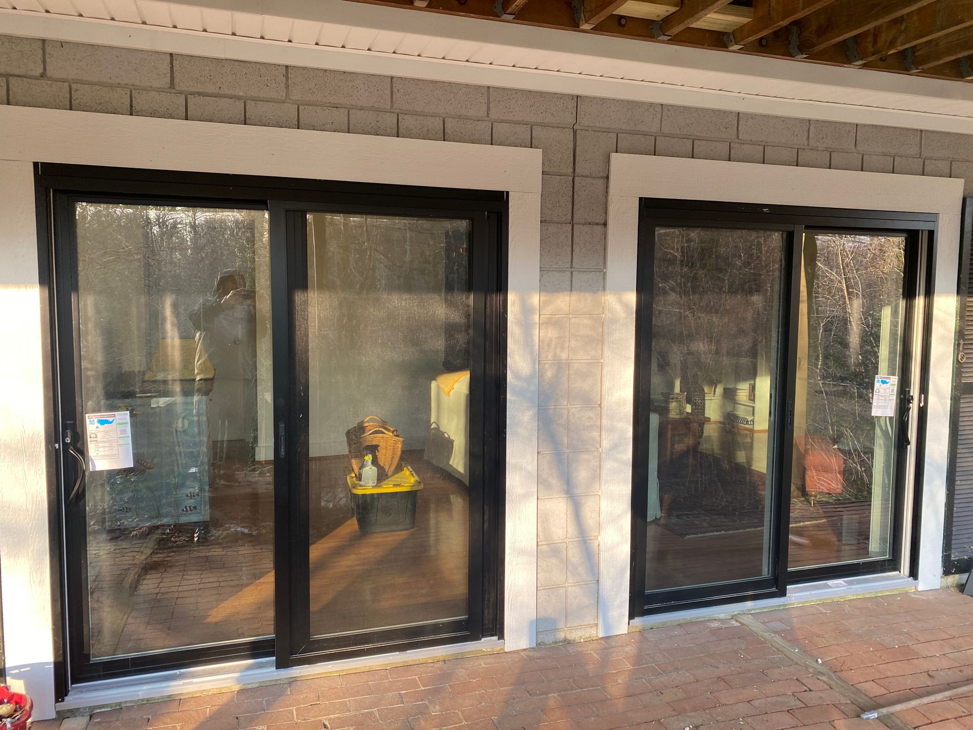 Storefront with two black-framed sliding glass doors and tan stone walls, reflecting sunlight on the sidewalk.