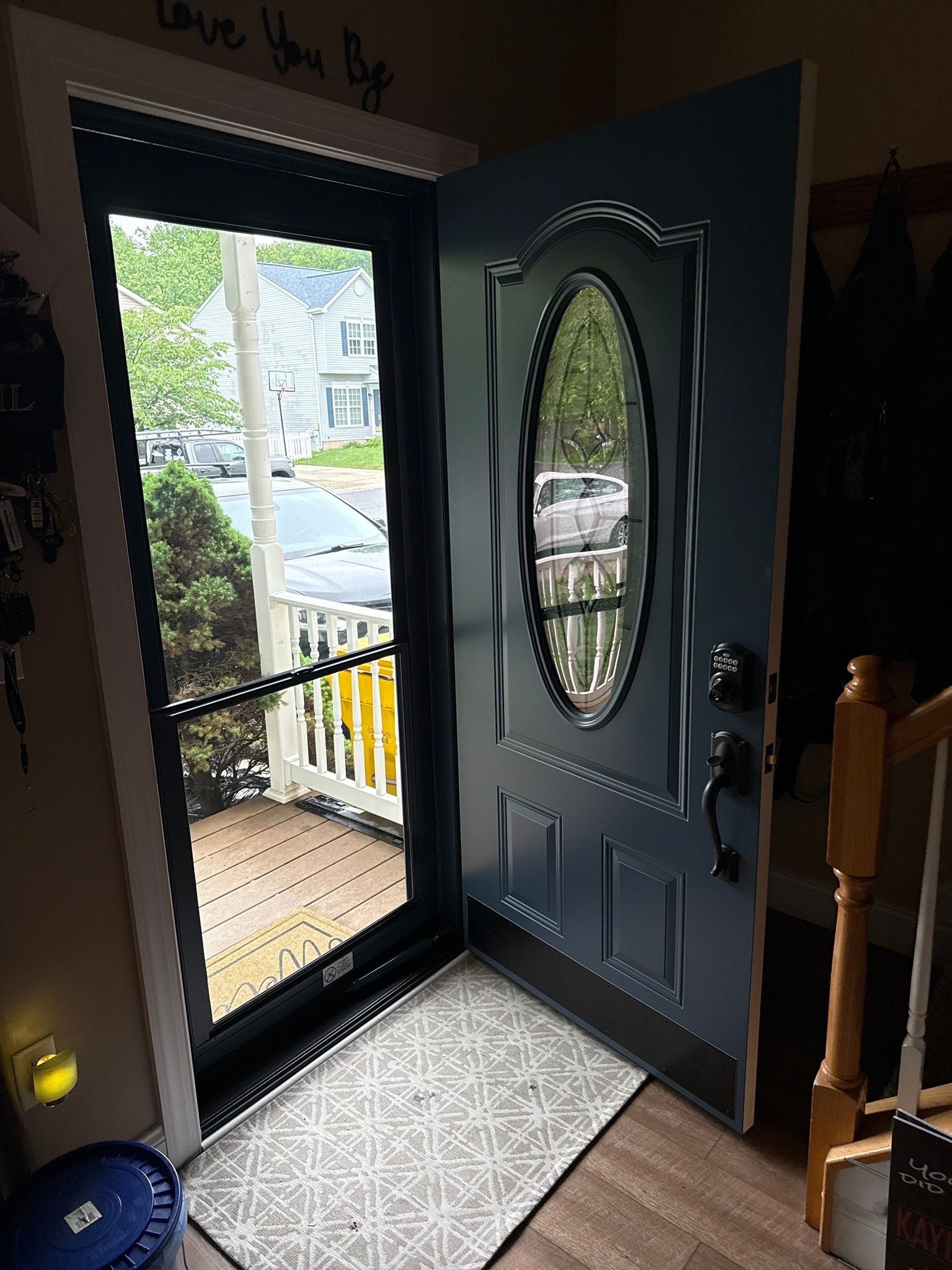 Open front door with oval glass, revealing a porch and parked car outside.