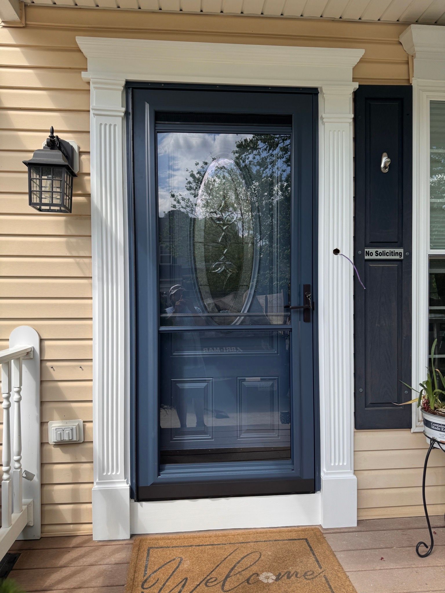 Front door with blue glass storm door, cream siding, porch light, and welcome mat under a covered porch.