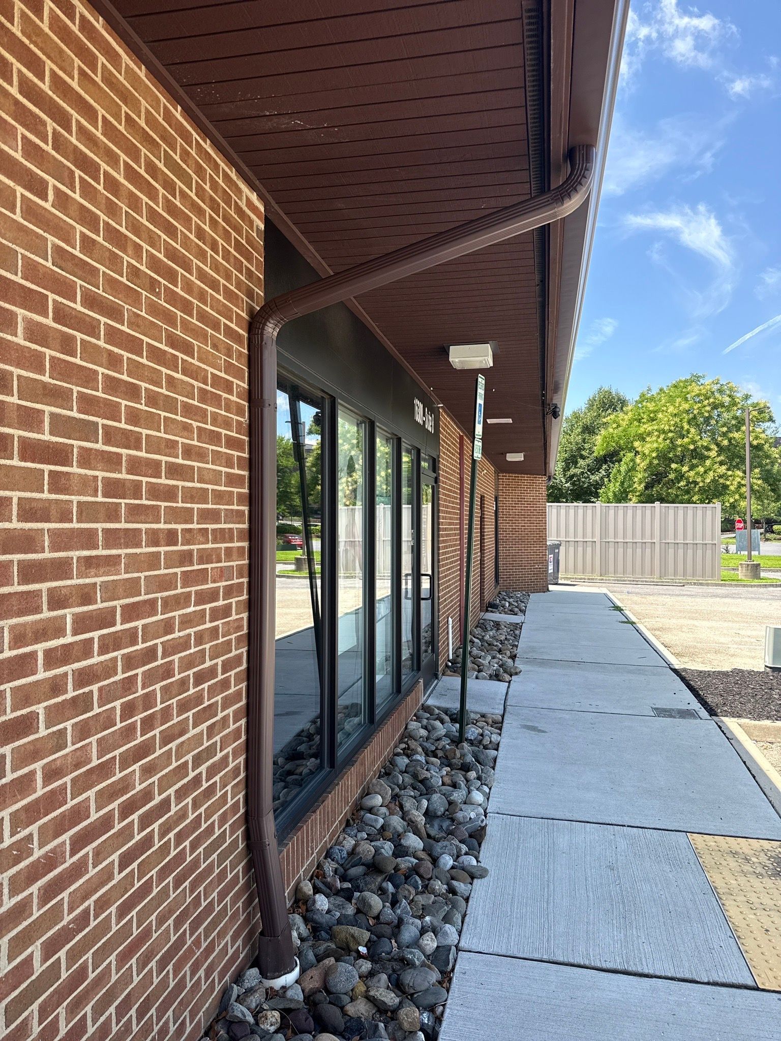 Brick building with glass windows, covered walkway, rock bed, and concrete path on a sunny day