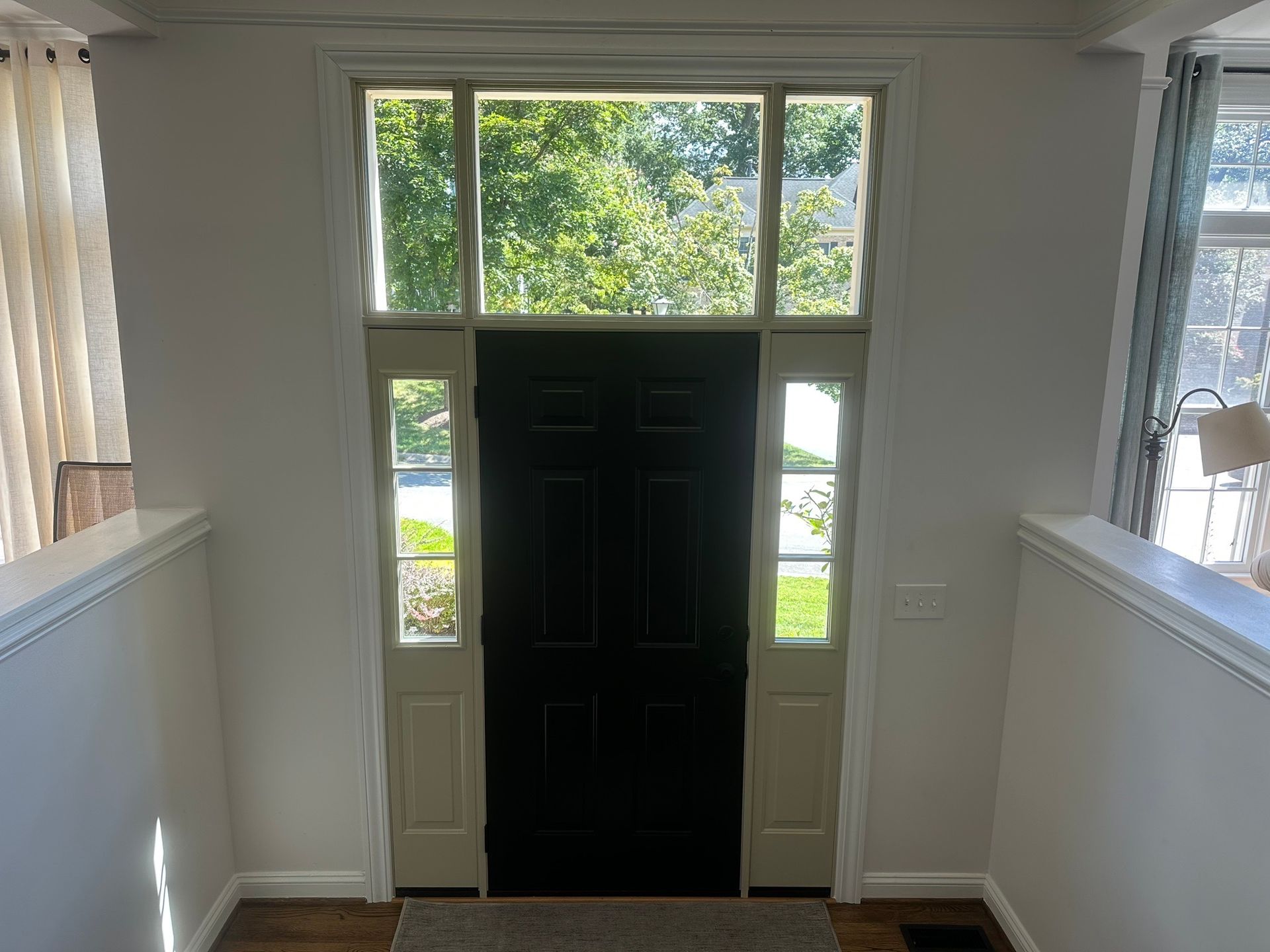 Front door with sidelights at the end of a bright hallway, with white walls and stairs on both sides