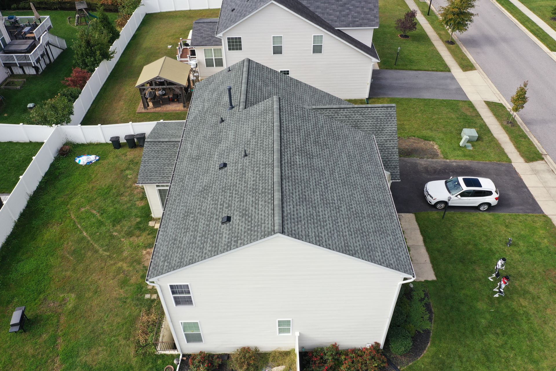 Aerial view of two white houses with gray roofs, a driveway, parked car, and a person on the lawn
