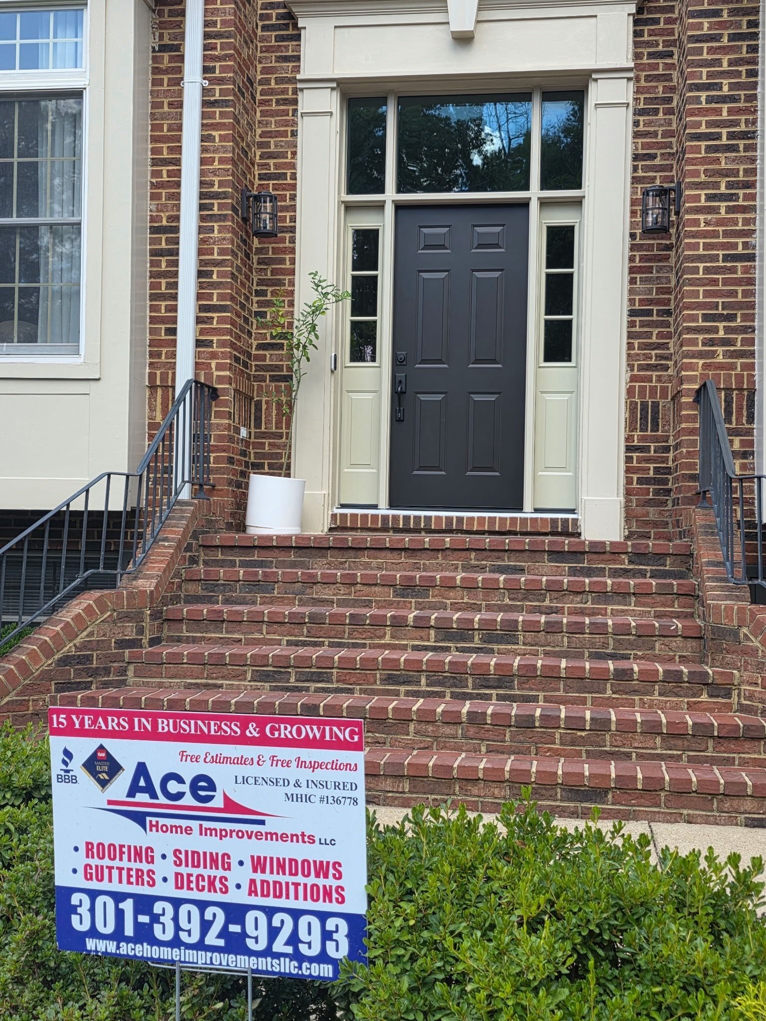 Brick house entry with dark front door and a lawn sign for Ace Restoration Services.