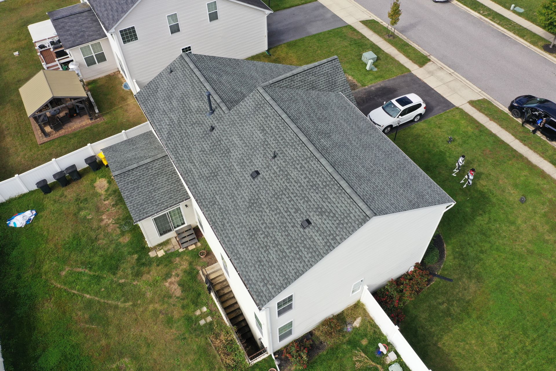 Aerial view of a white house with a gray roof, driveway, and parked car in a suburban neighborhood.