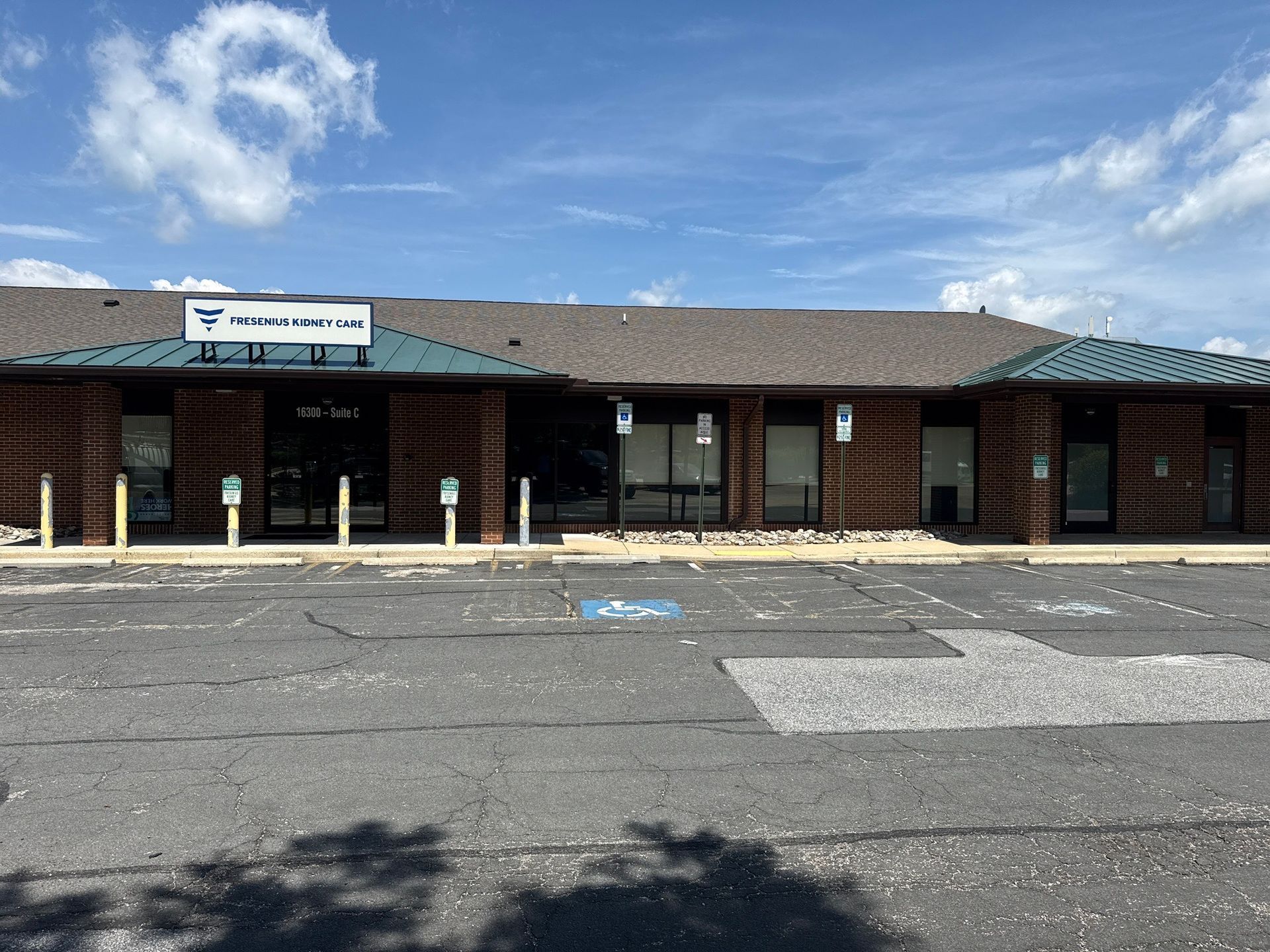 Single-story brick storefront with a sign, boarded windows, and an empty parking lot under a blue sky.