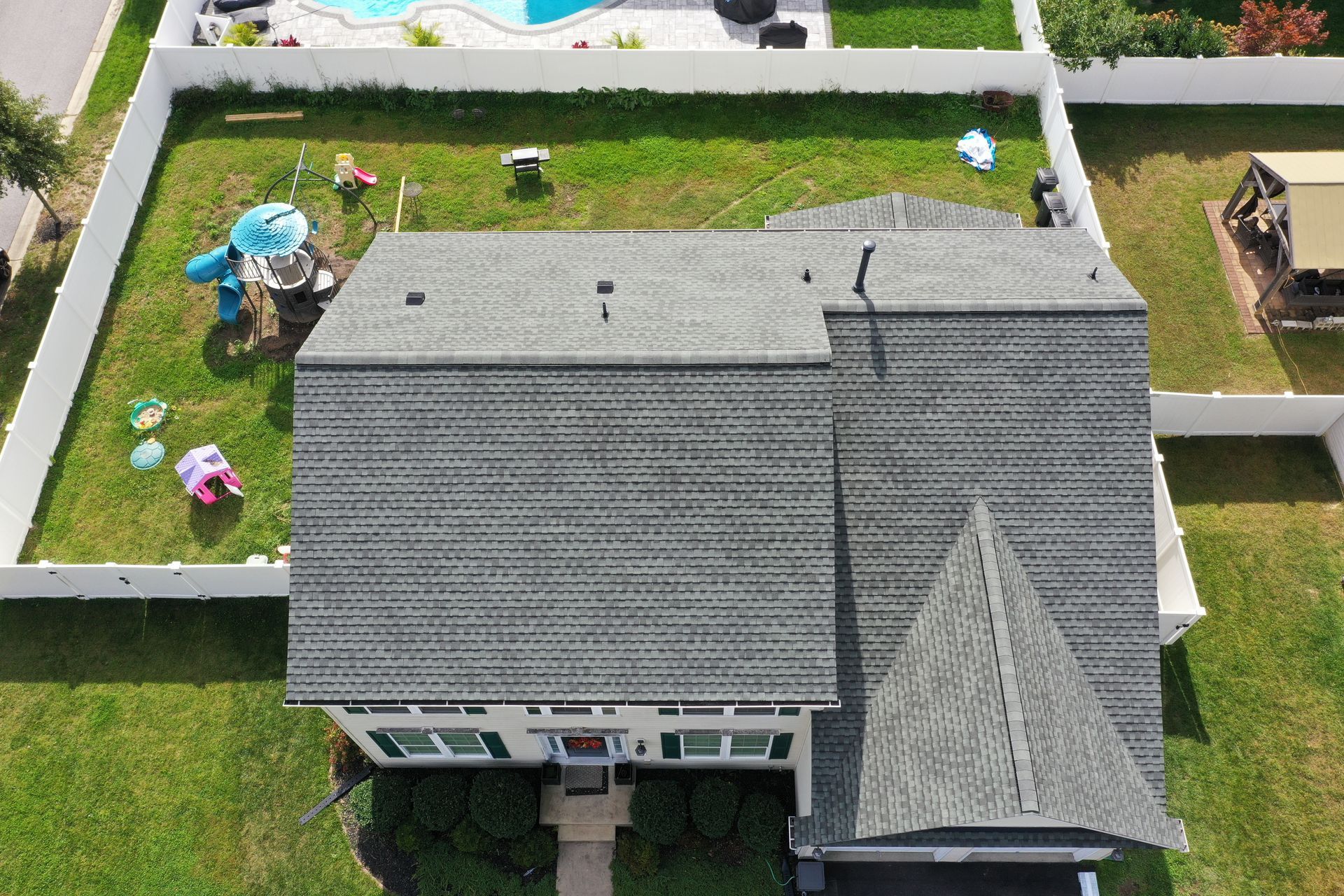 Aerial view of a house with gray shingles and a small fenced yard with play equipment.