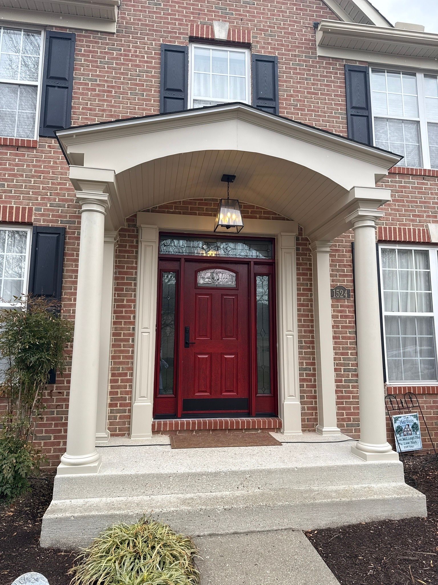 Brick house entrance with red front door, white columns, and arched porch roof