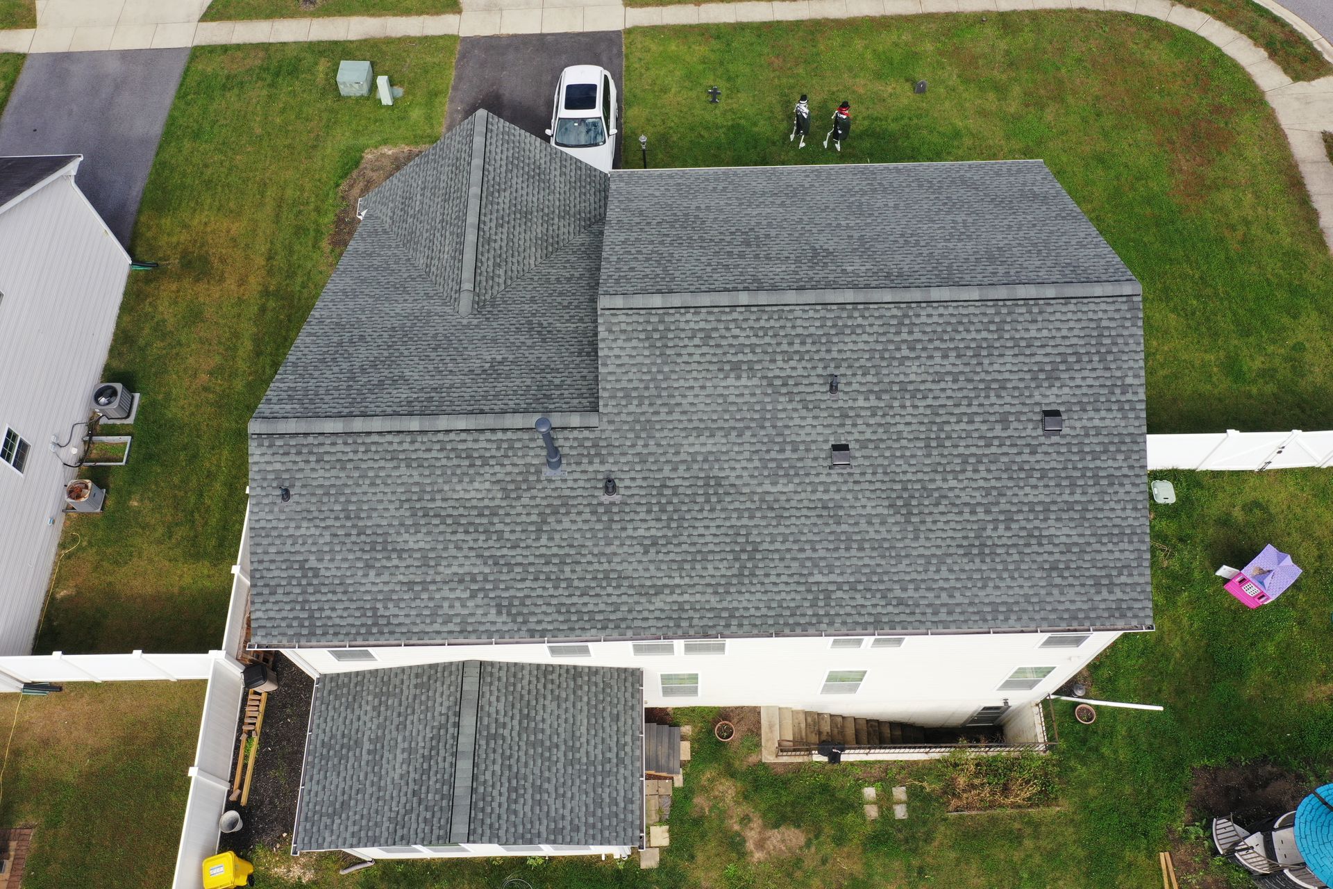 Aerial view of a gray-roofed suburban house with yard, driveway, and parked vehicle.