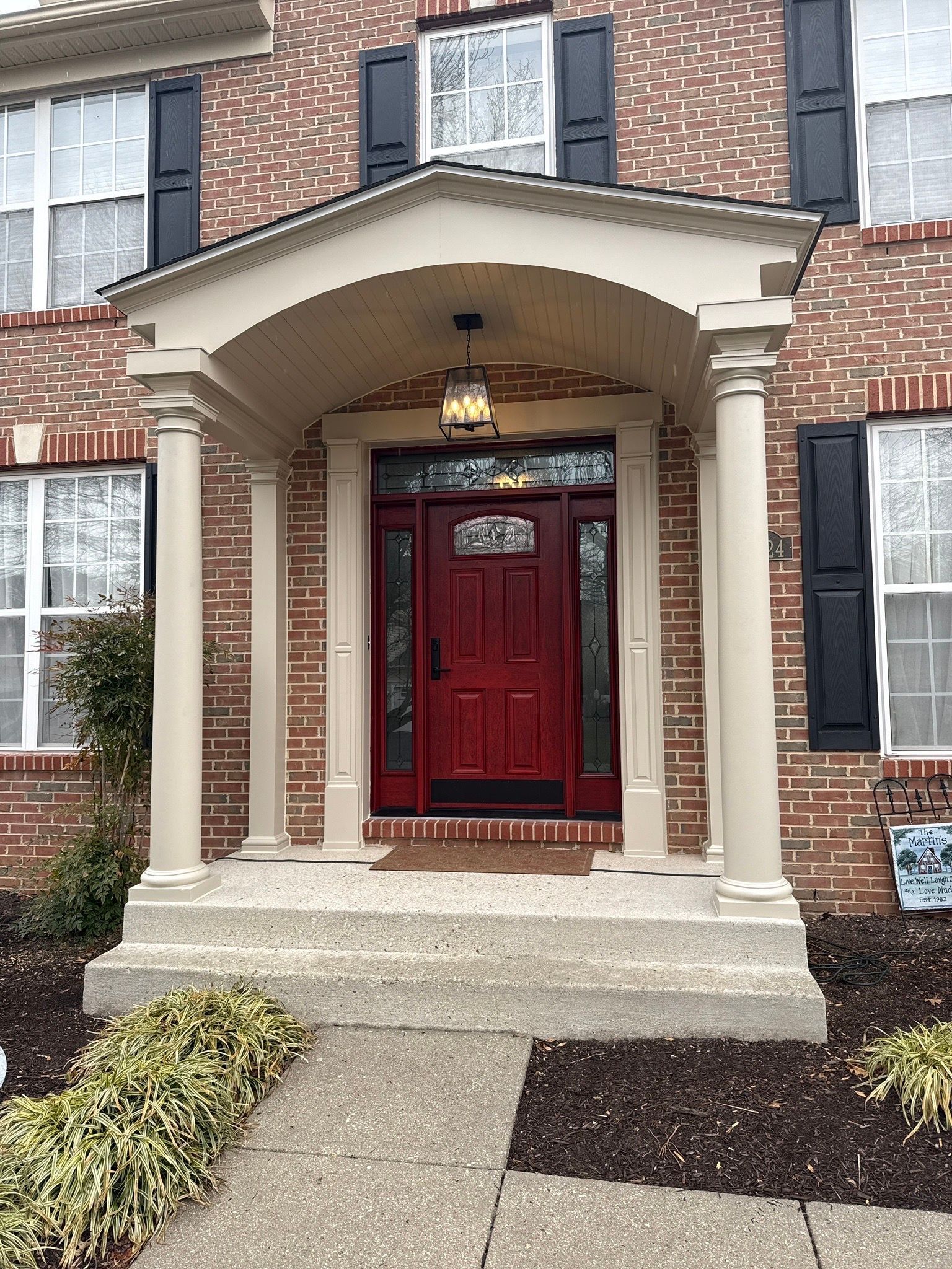 Brick house entry with red front door, arched porch, and concrete walkway.