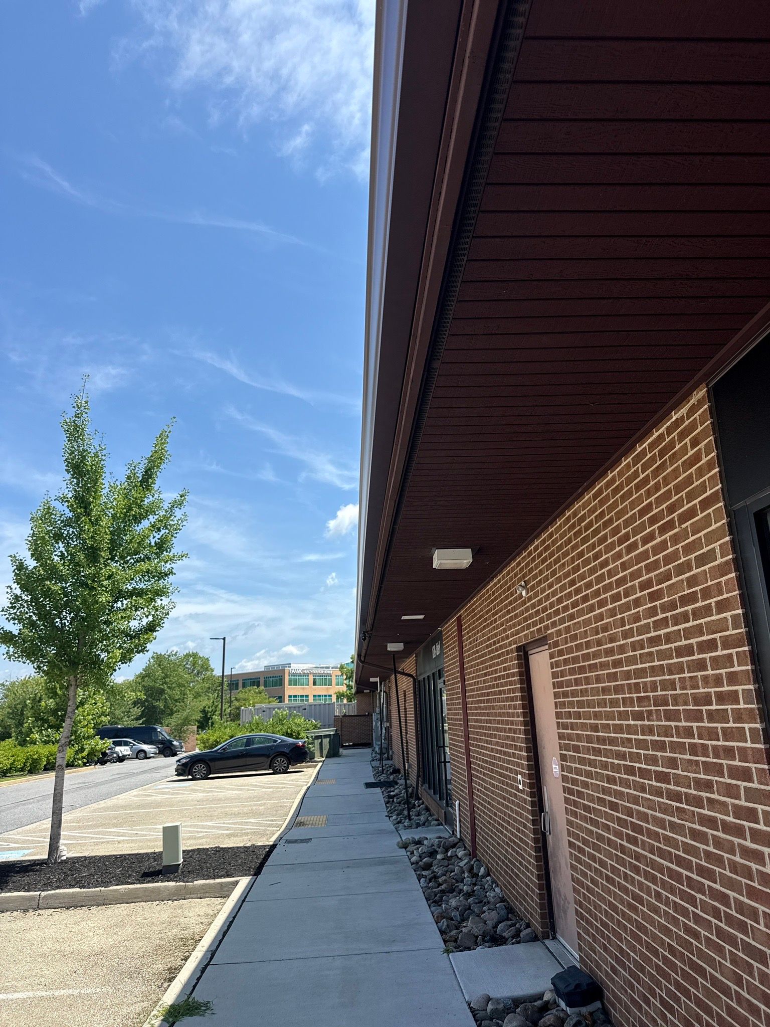 Brick building with sidewalk, parked cars, and a tree under a clear blue sky