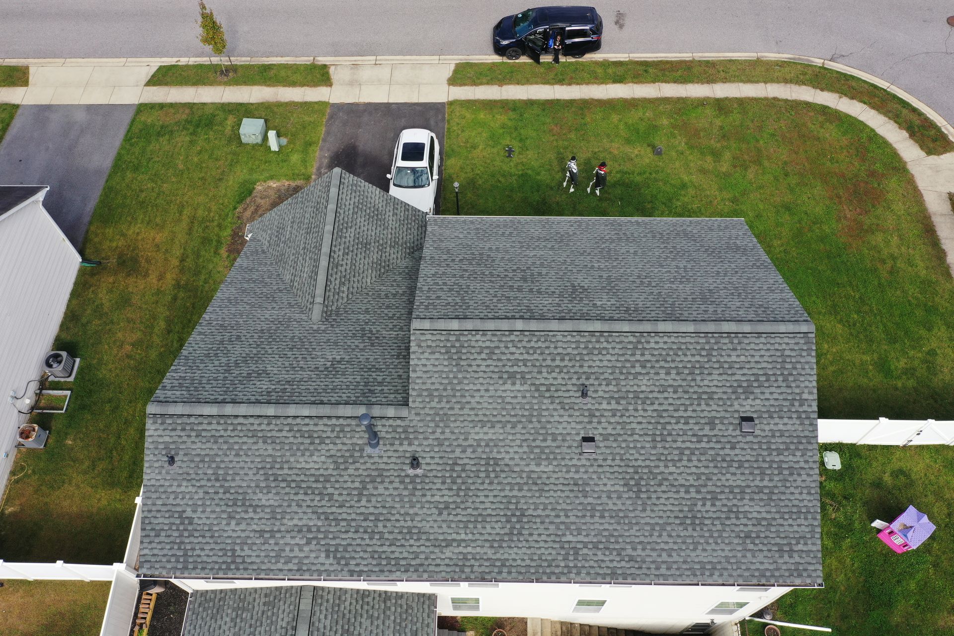 Aerial view of a gray-roofed house with a driveway, parked cars, and green lawn.