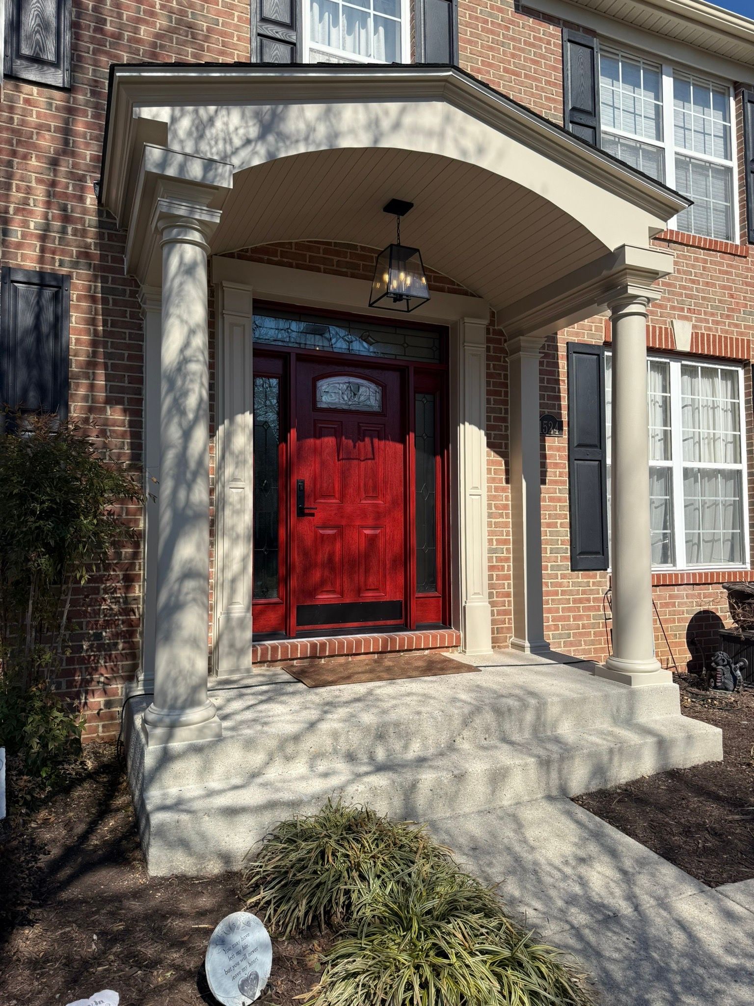 Front entrance with red door, arched porch, brick facade, and stone steps in bright sunlight