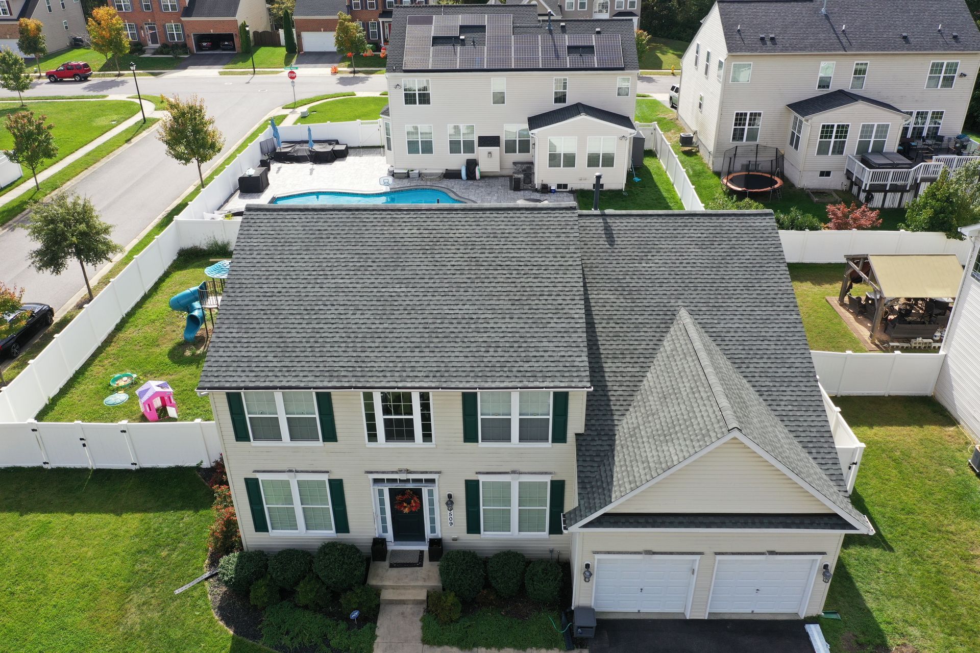 Aerial view of a two-story white house with gray roof, attached garage, and backyard pool in a suburban neighborhood