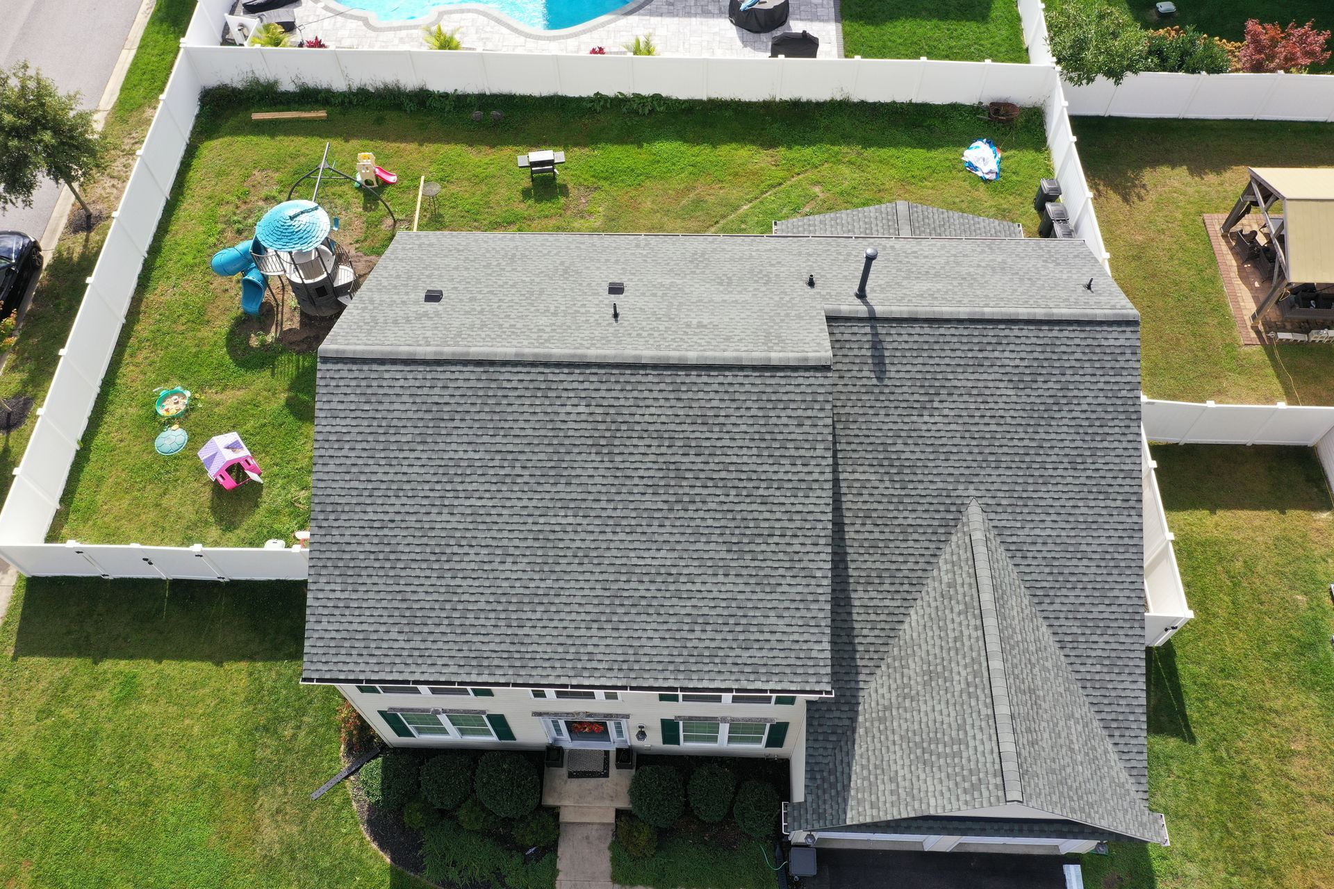 Aerial view of a gray-roofed house with a landscaped backyard and a small pool nearby.