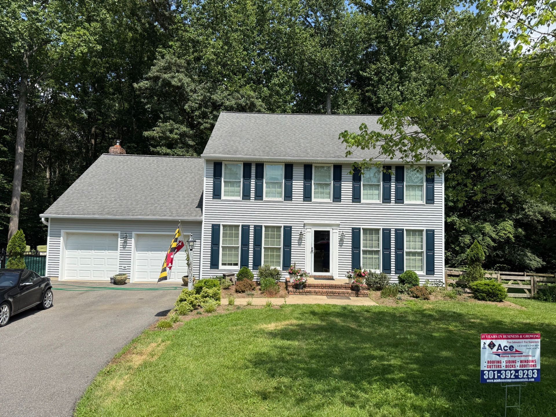 Two-story white house with blue shutters and attached garage, seen from a front lawn on a sunny day