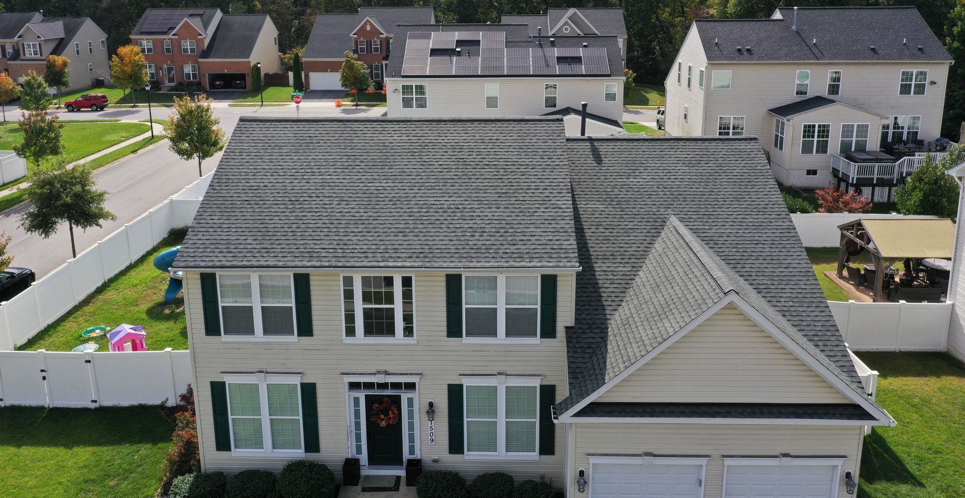 Aerial view of a two-story beige house with a gray roof and garage in a suburban neighborhood