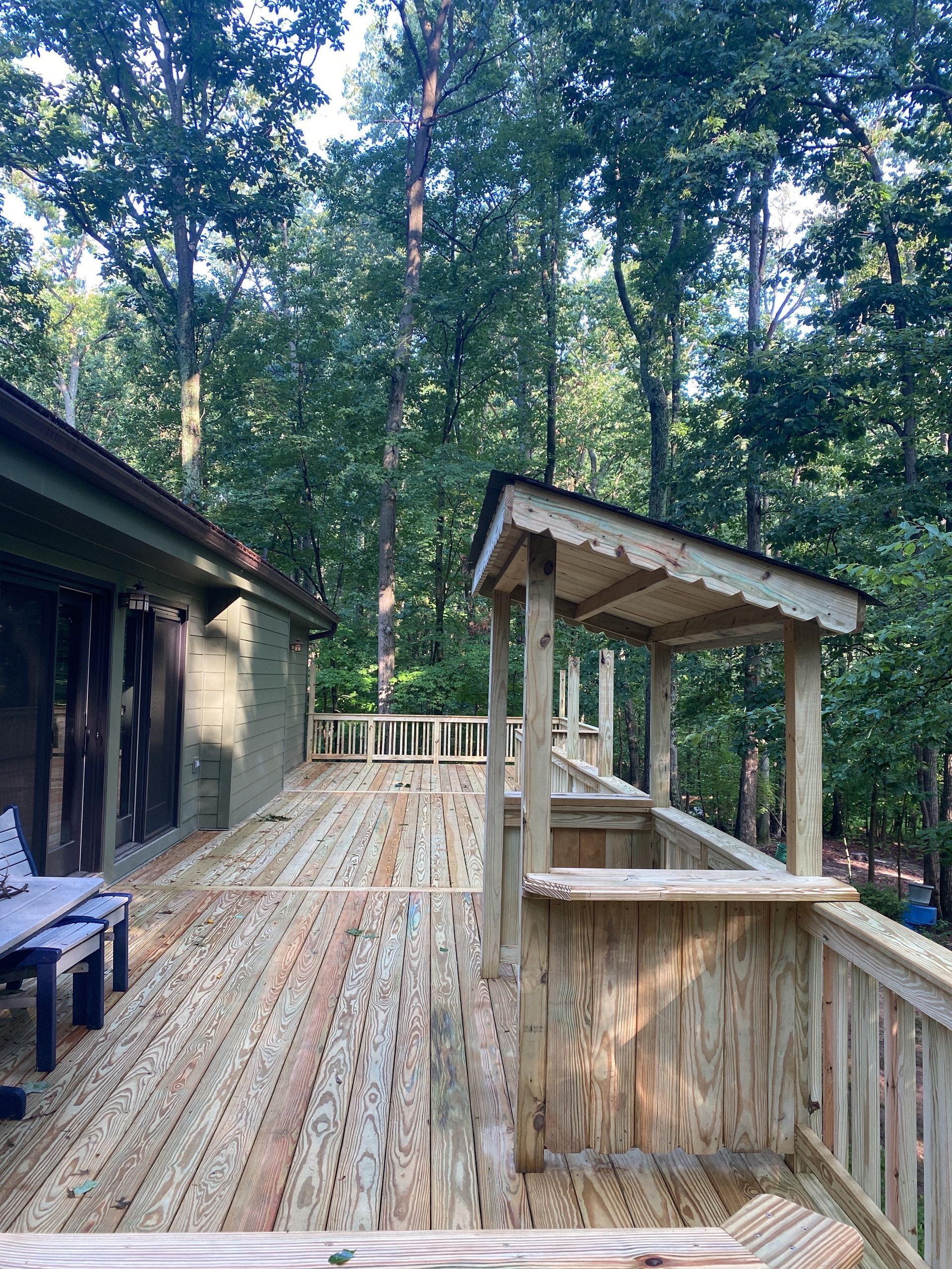 Wooden deck with railing beside a cabin in a forest, surrounded by tall trees