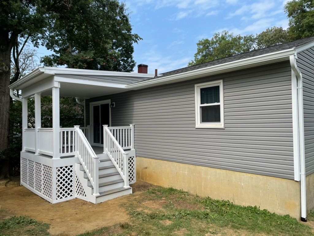 Gray house exterior with white porch, lattice skirting, and front steps under a partly cloudy sky