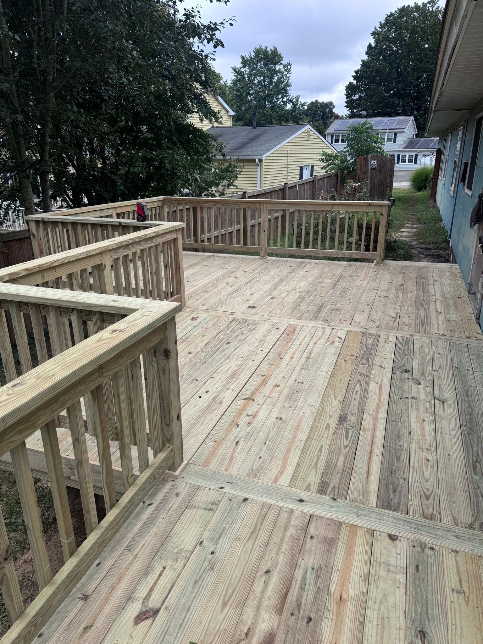 Wooden deck with railings overlooking a yard and neighboring houses under cloudy skies