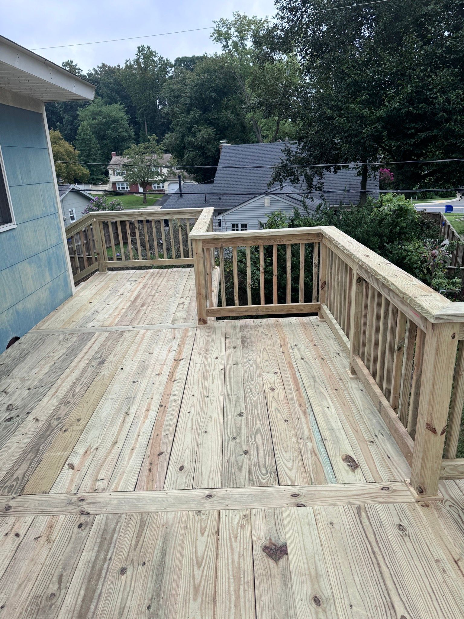 Wooden deck under construction beside a house, with railings and stairs leading down to a yard.