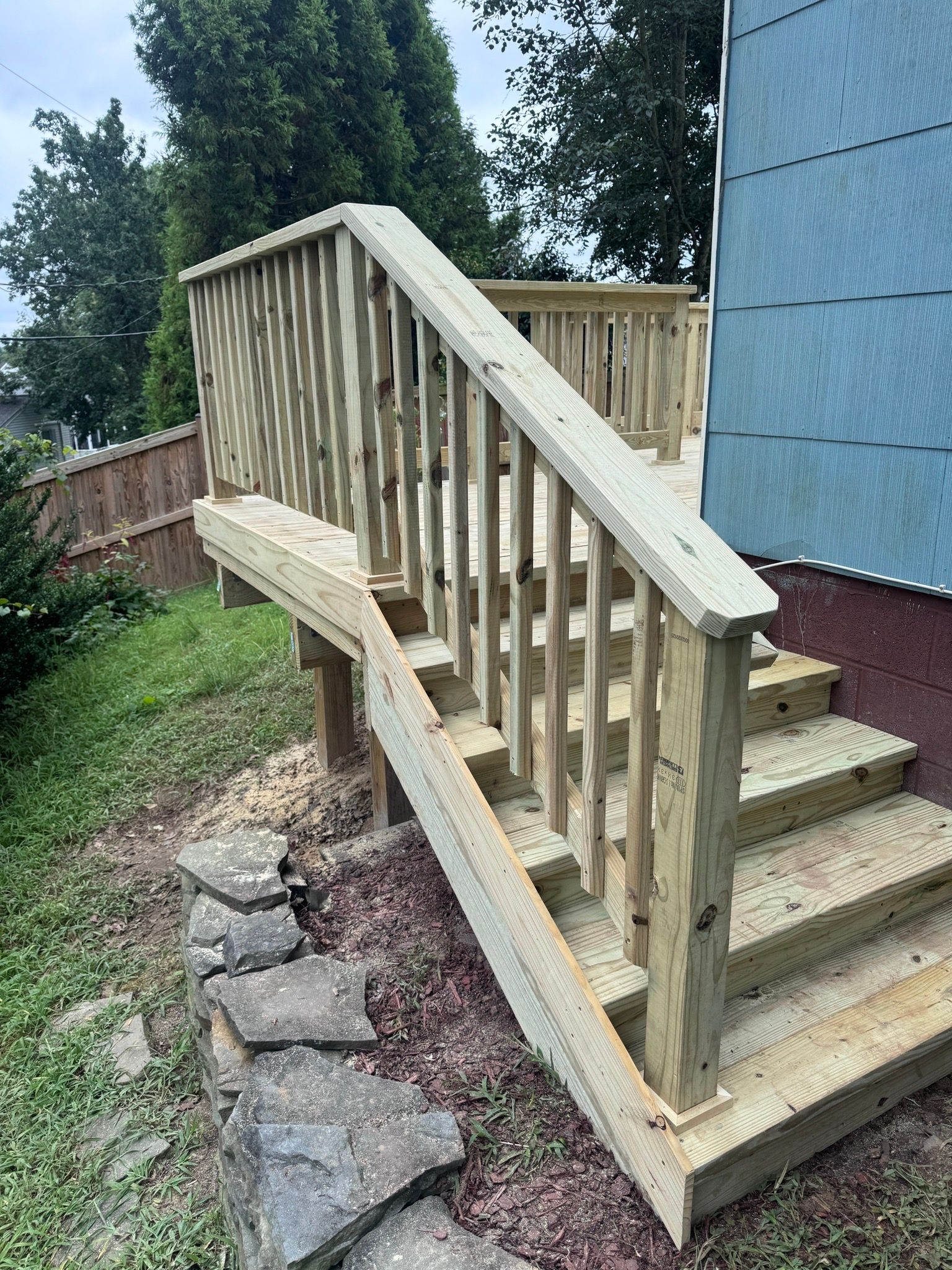 Wooden accessibility ramp with railings leading to a house entrance beside stone steps and grass.