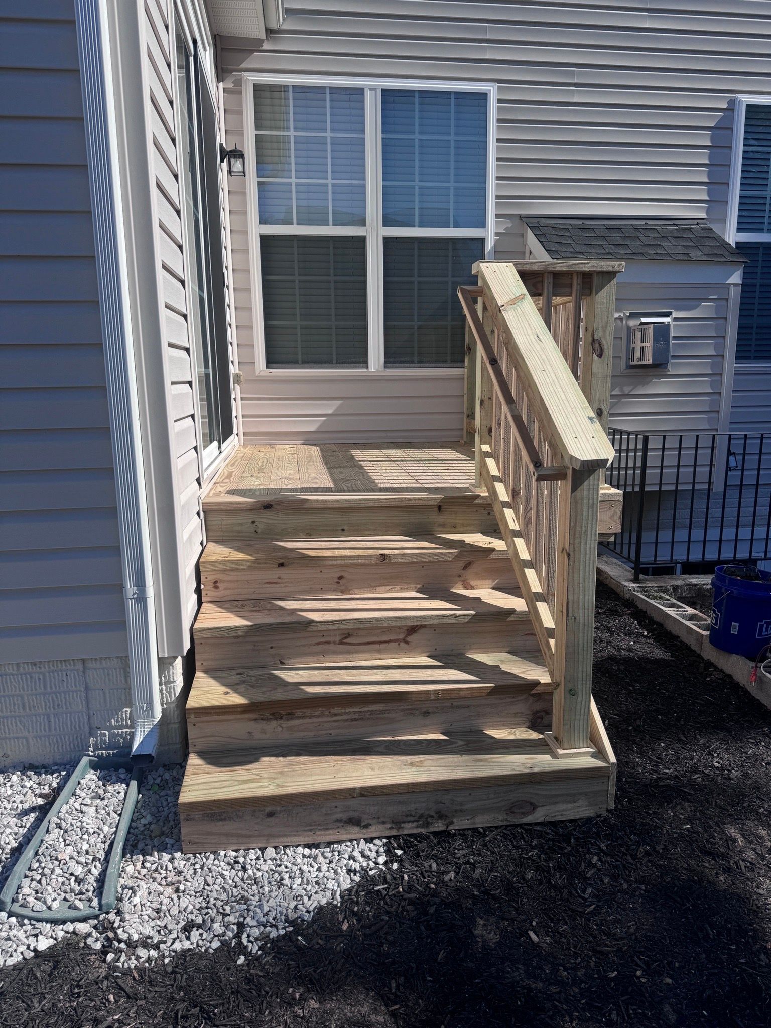 Wooden porch ramp with railings leading to a house entrance beside gray siding.