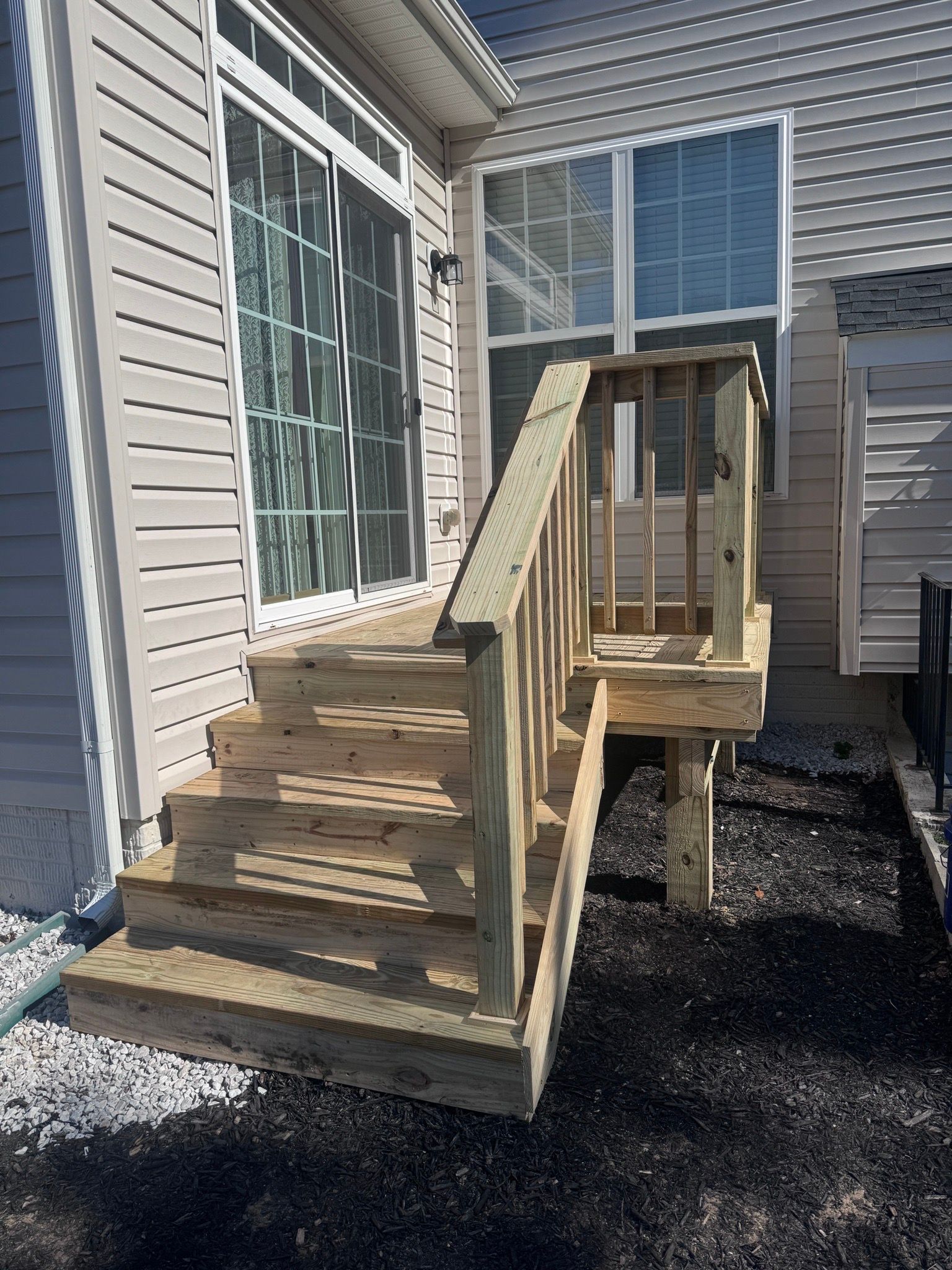 Wooden front steps and ramp beside a house with beige siding and large windows.