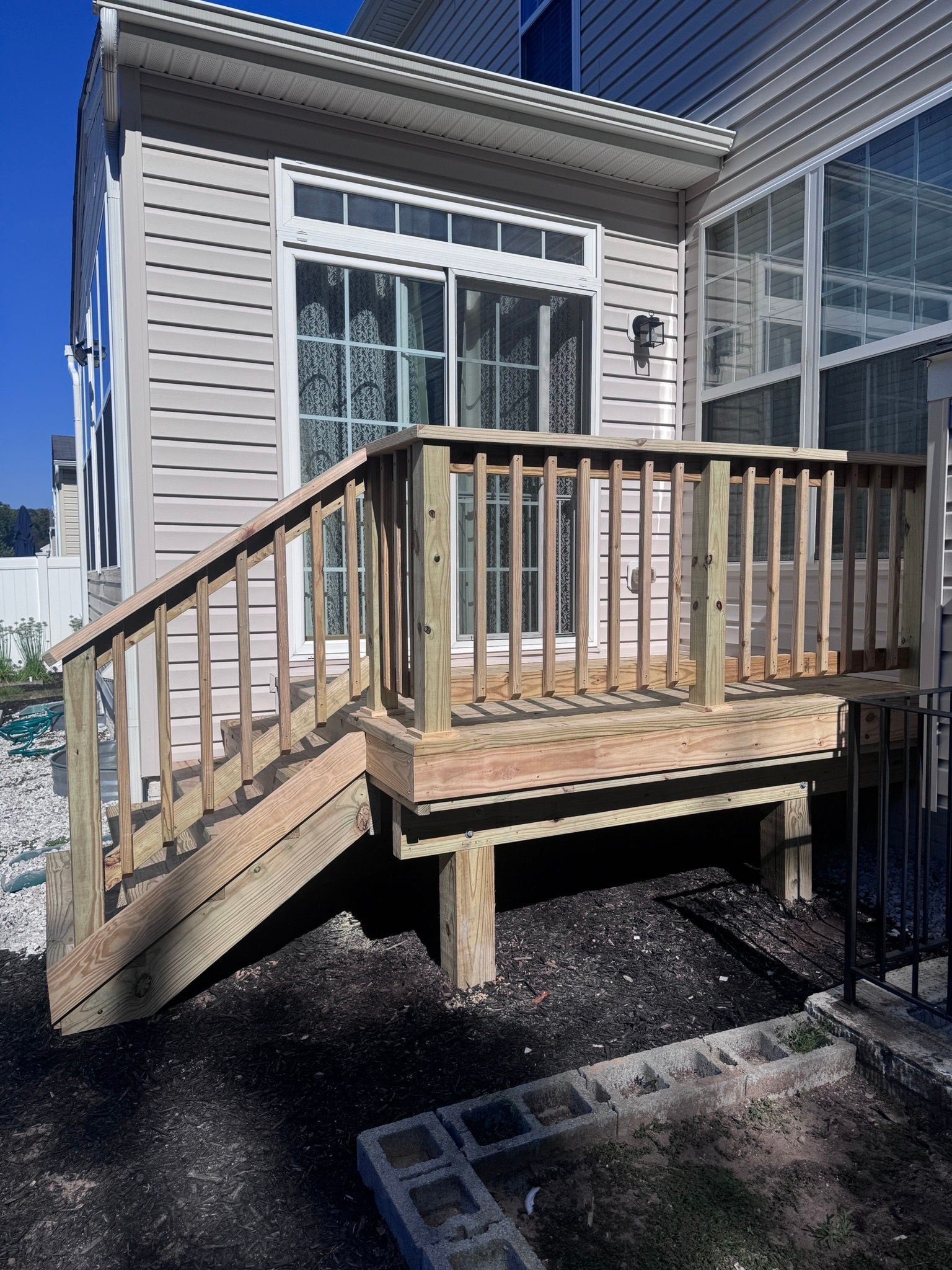 Wooden ramp leading to a small raised deck beside a beige building with a window and railing.
