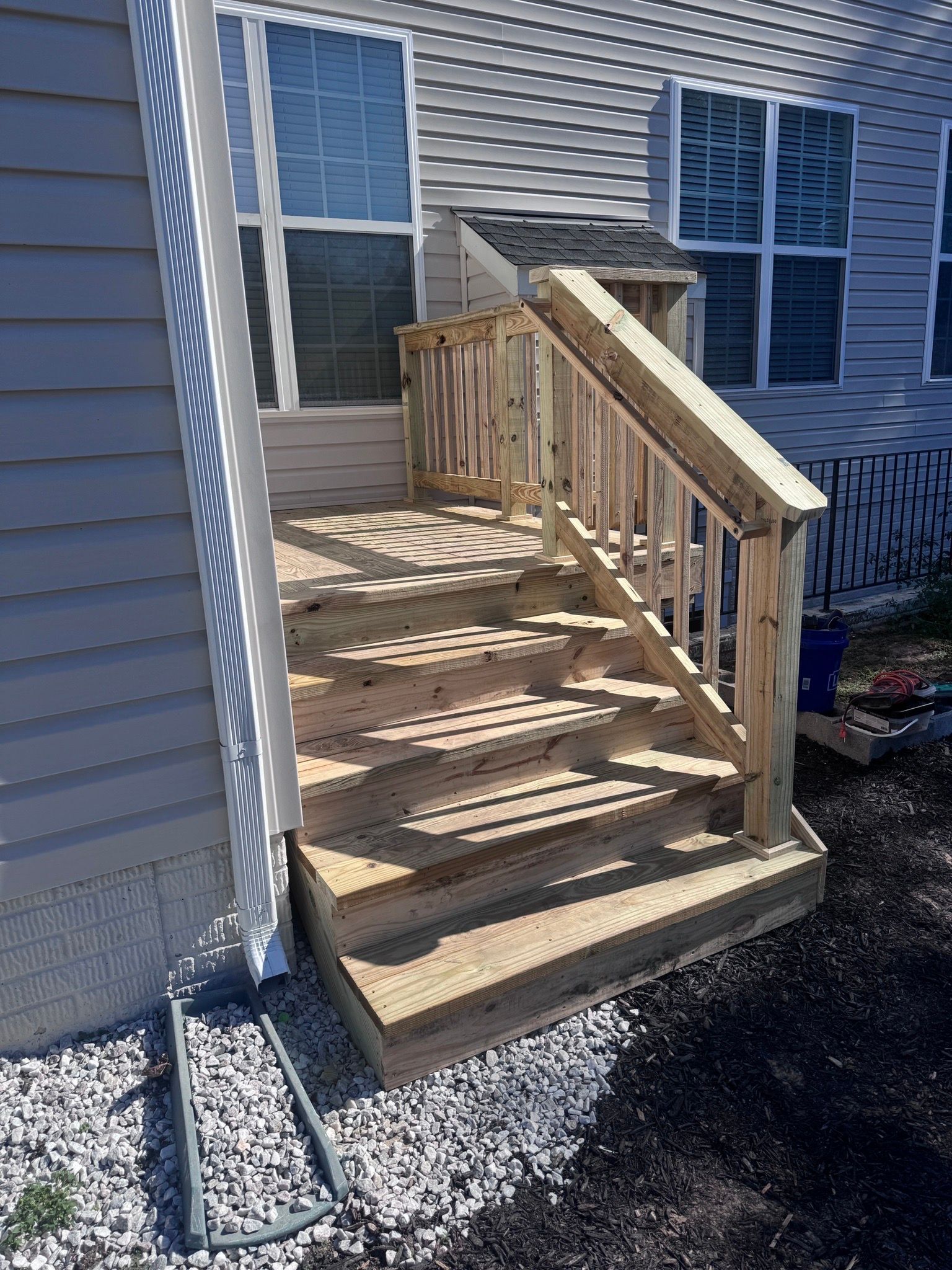 Wooden porch steps with railing leading to a house entrance beside blue siding and windows.