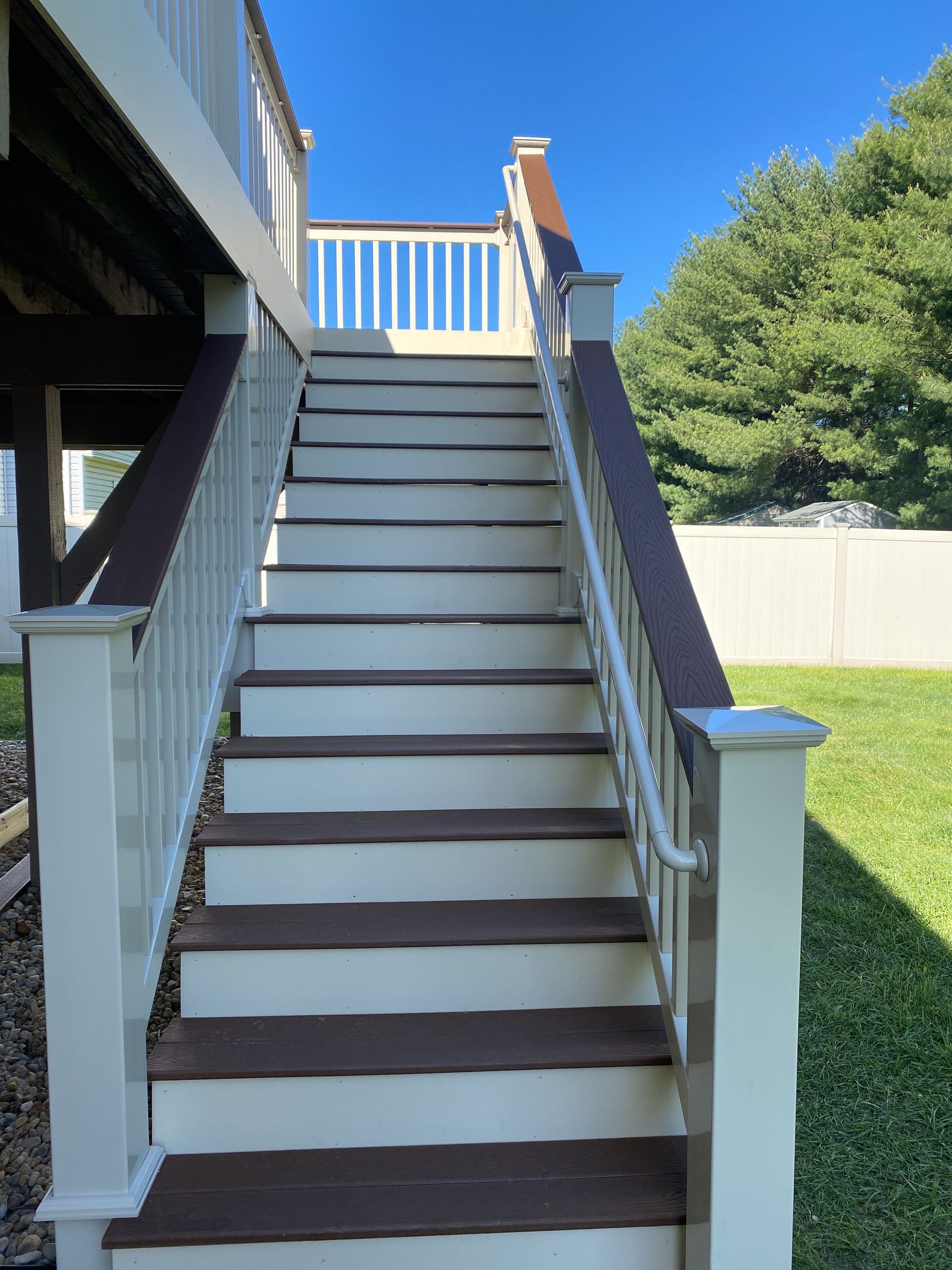 Outdoor wooden staircase with dark treads, white railings, and a lawn beside a house.