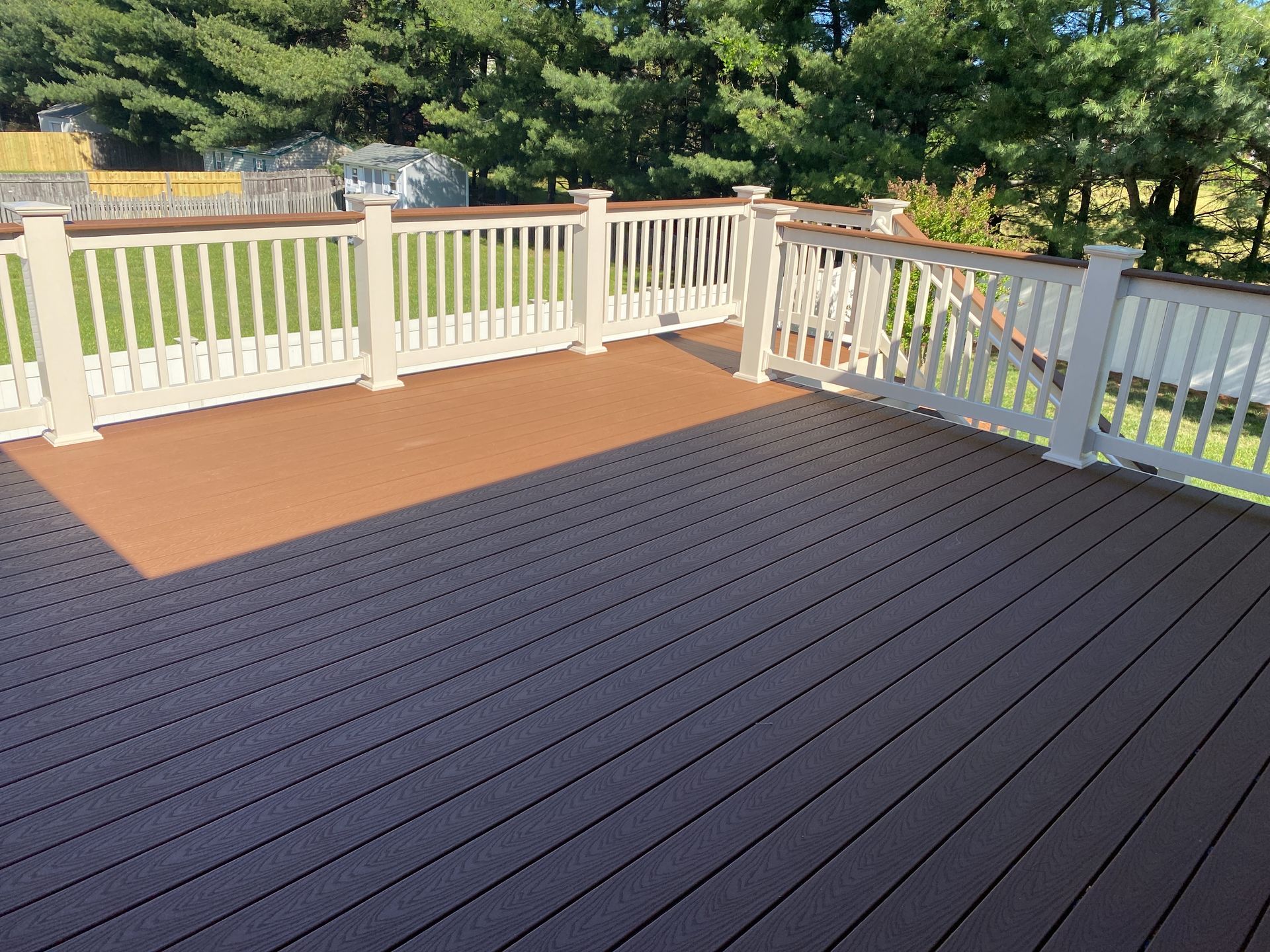 White-railed backyard deck with gray composite flooring and a brown mat, overlooking trees and grass