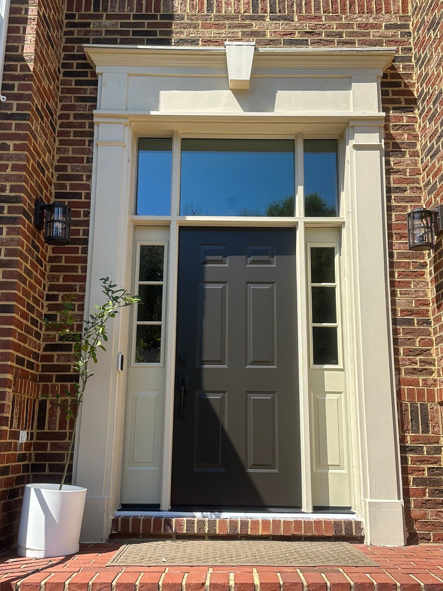 Front entrance of a brick house with a dark door, white trim, and side windows.