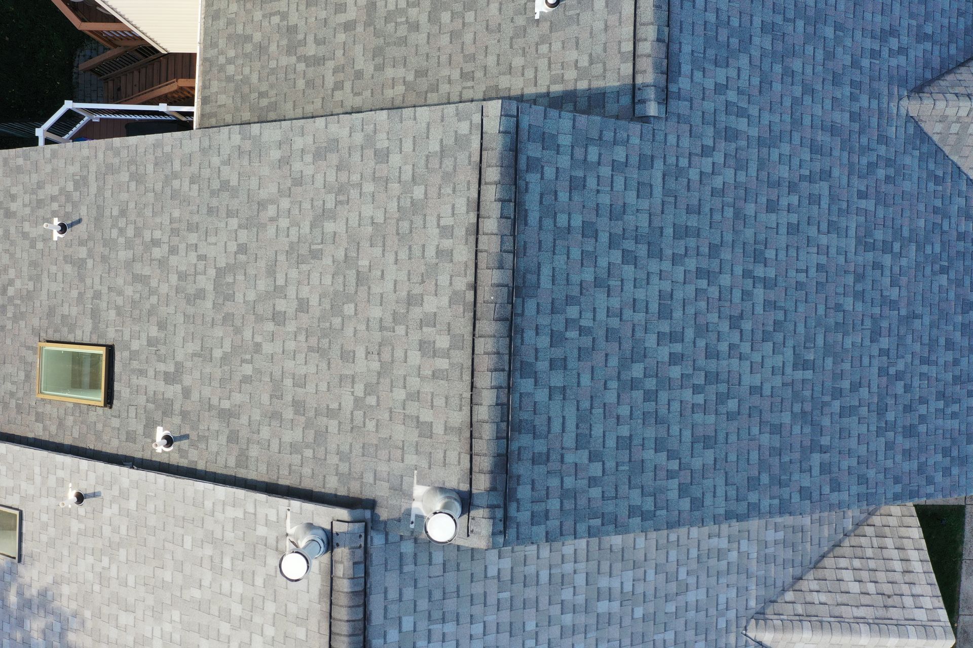 Aerial view of gray and blue shingled rooftops with skylights and vents.