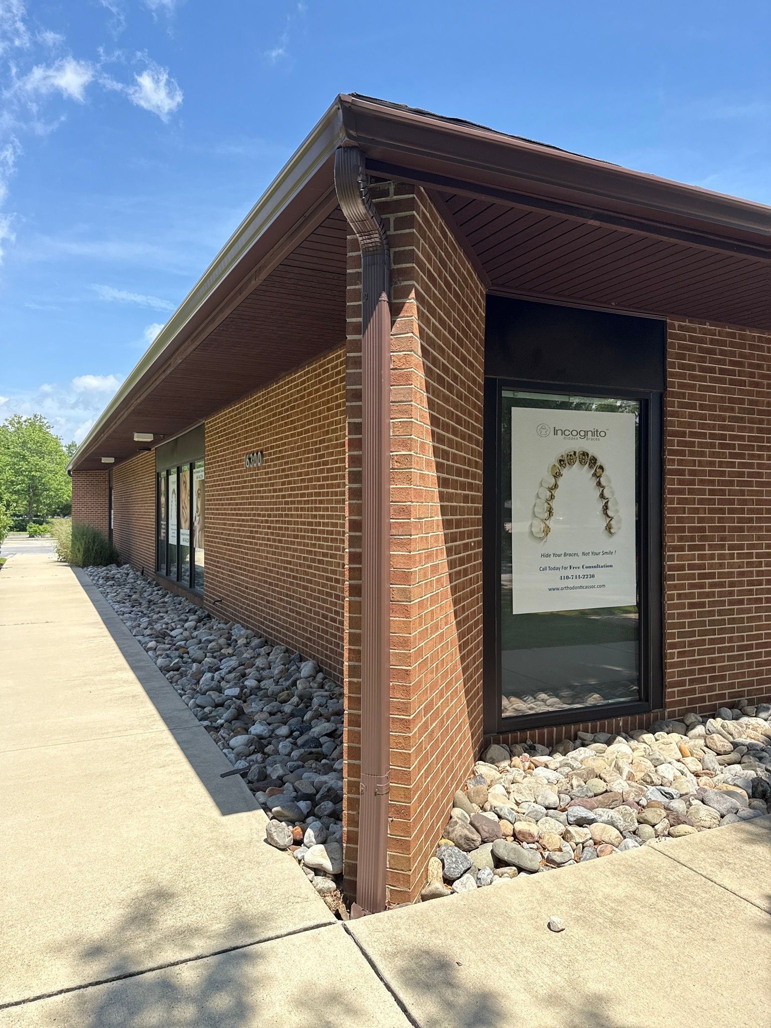 Brick building with patterned wall, glass door, and a sunlit sidewalk under a blue sky.