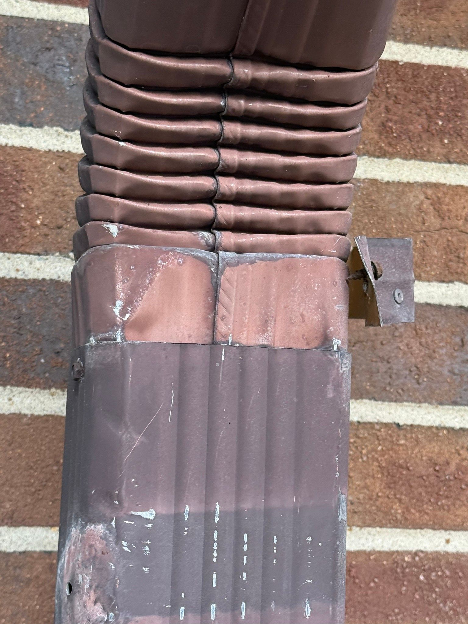 Brown vent pipe with wrapped base and weathered metal flashing on a brick surface