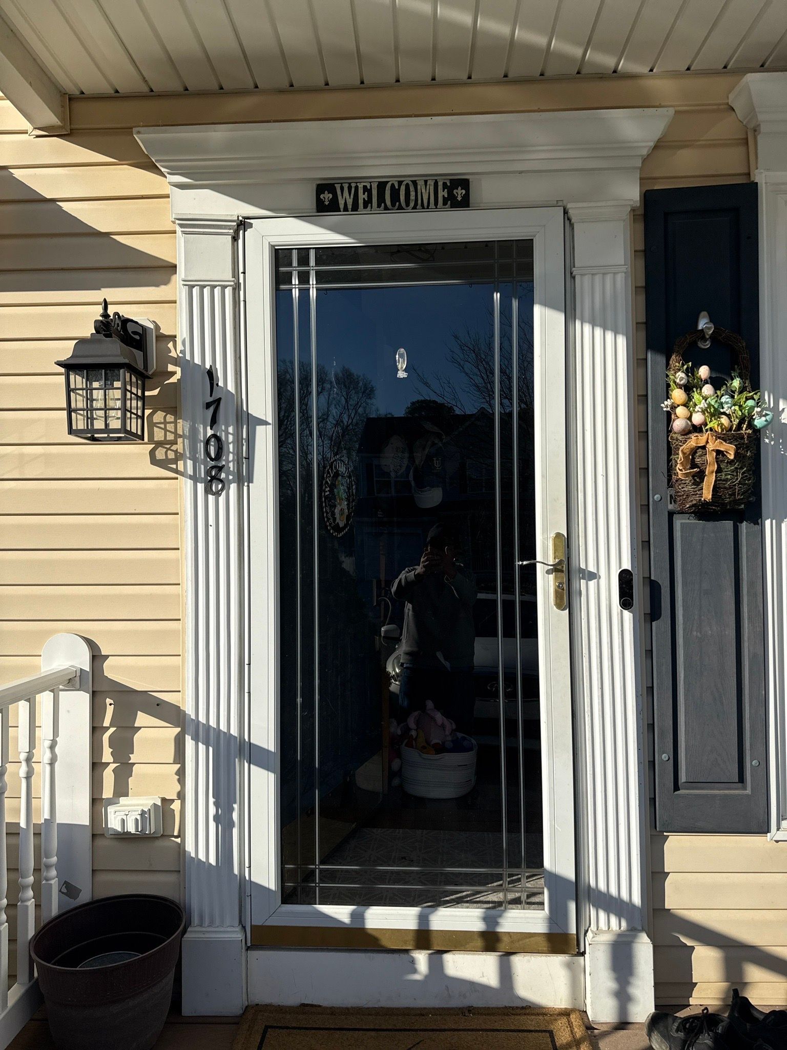 Front porch with a glass storm door, white trim, beige siding, and hanging flower basket.