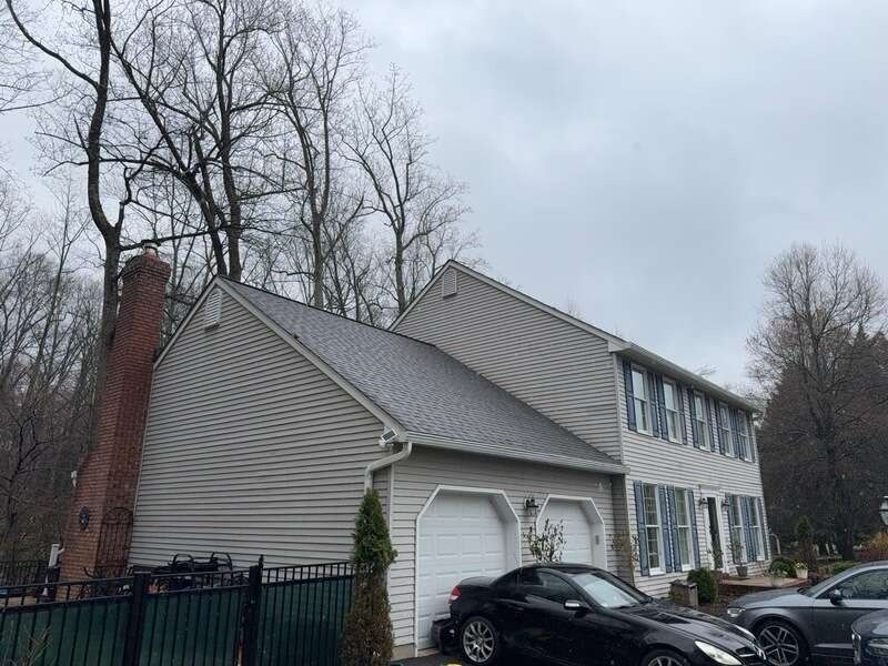 Suburban townhouse with gray siding, white garage, brick chimney, and parked cars under bare trees