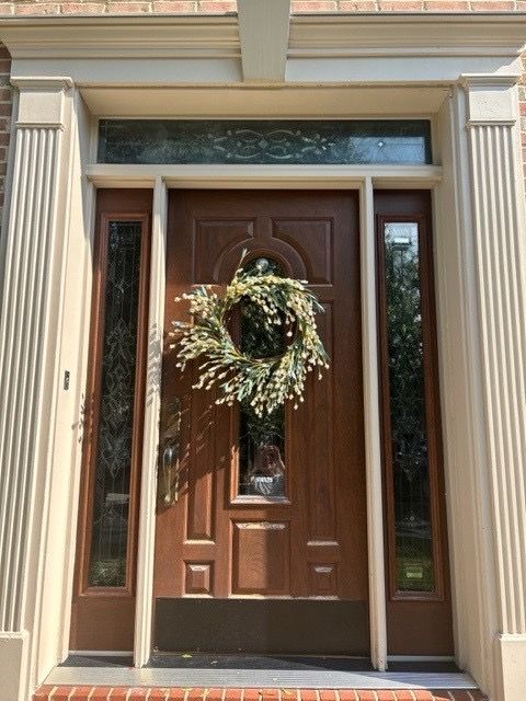 Front door with a wreath, flanked by narrow sidelights and cream trim at a house entrance.